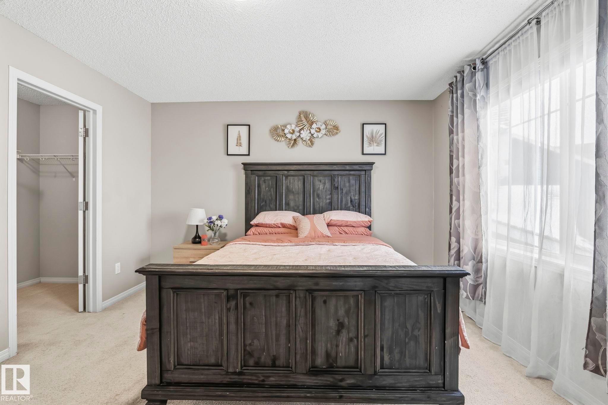 Bedroom featuring light-colored carpet, a large window with sheer and patterned curtains, and an open closet with wire shelving - 4783 Crabapplle Run, Edmonton, AB - Indoor Photo Showing Bedroom