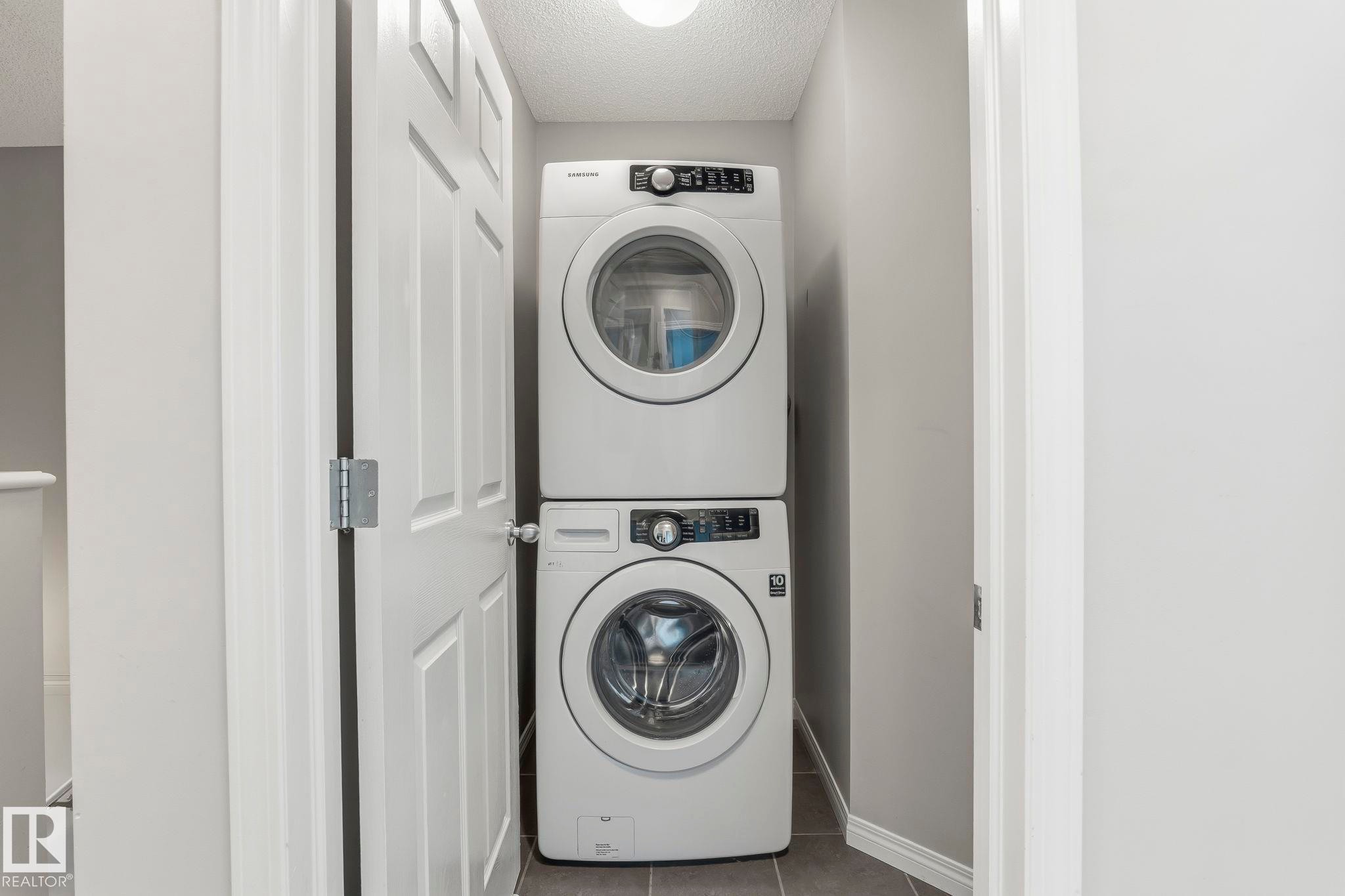 Dedicated laundry area featuring a white stackable washer and dryer unit, set against light gray walls with a matching baseboard, and dark gray tiled flooring - 4783 Crabapplle Run, Edmonton, AB - Indoor Photo Showing Laundry Room