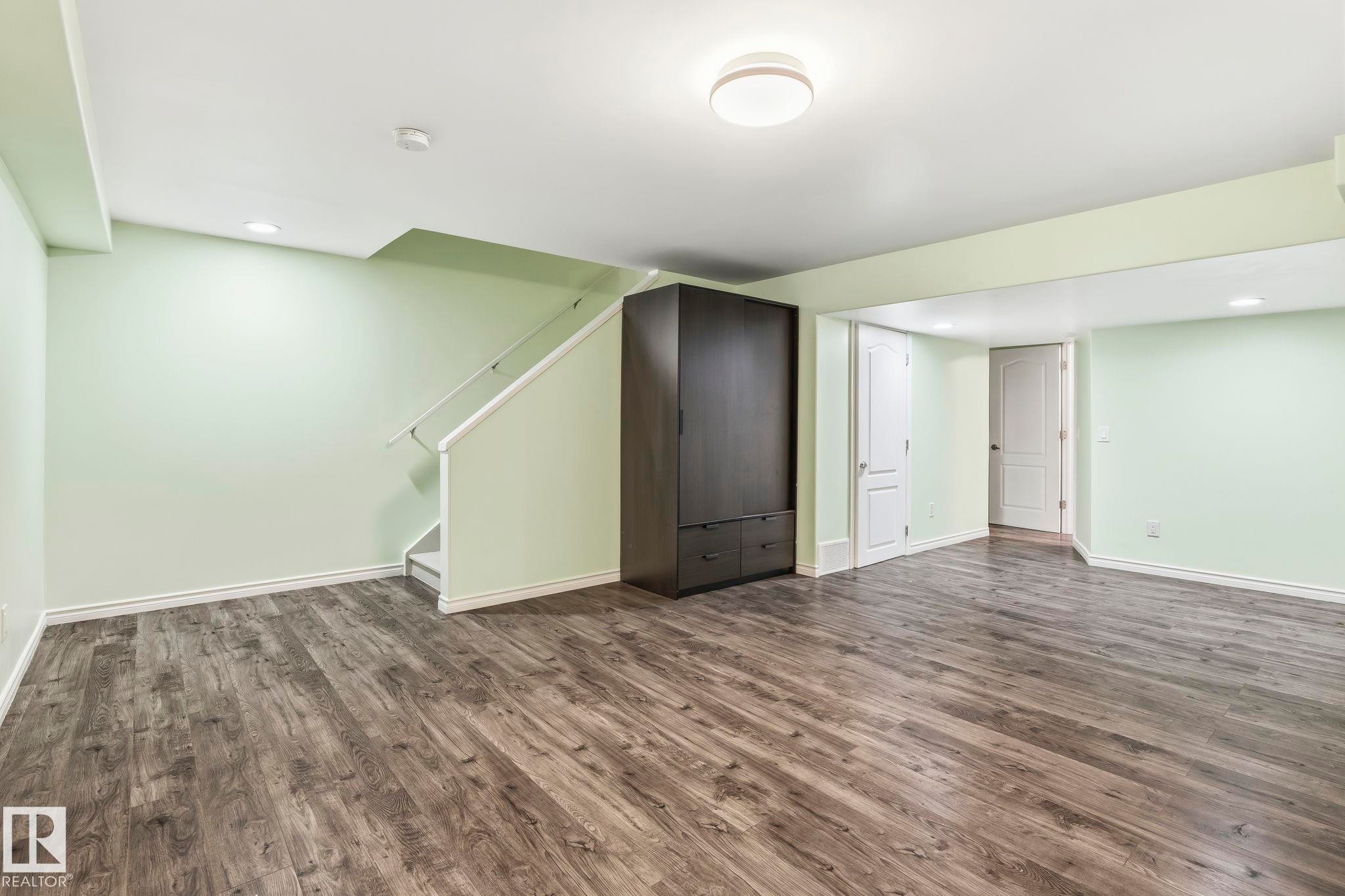 Spacious room featuring wood-look flooring, light green walls, and a recessed ceiling light - 4783 Crabapplle Run, Edmonton, AB - Indoor Photo Showing Other Room