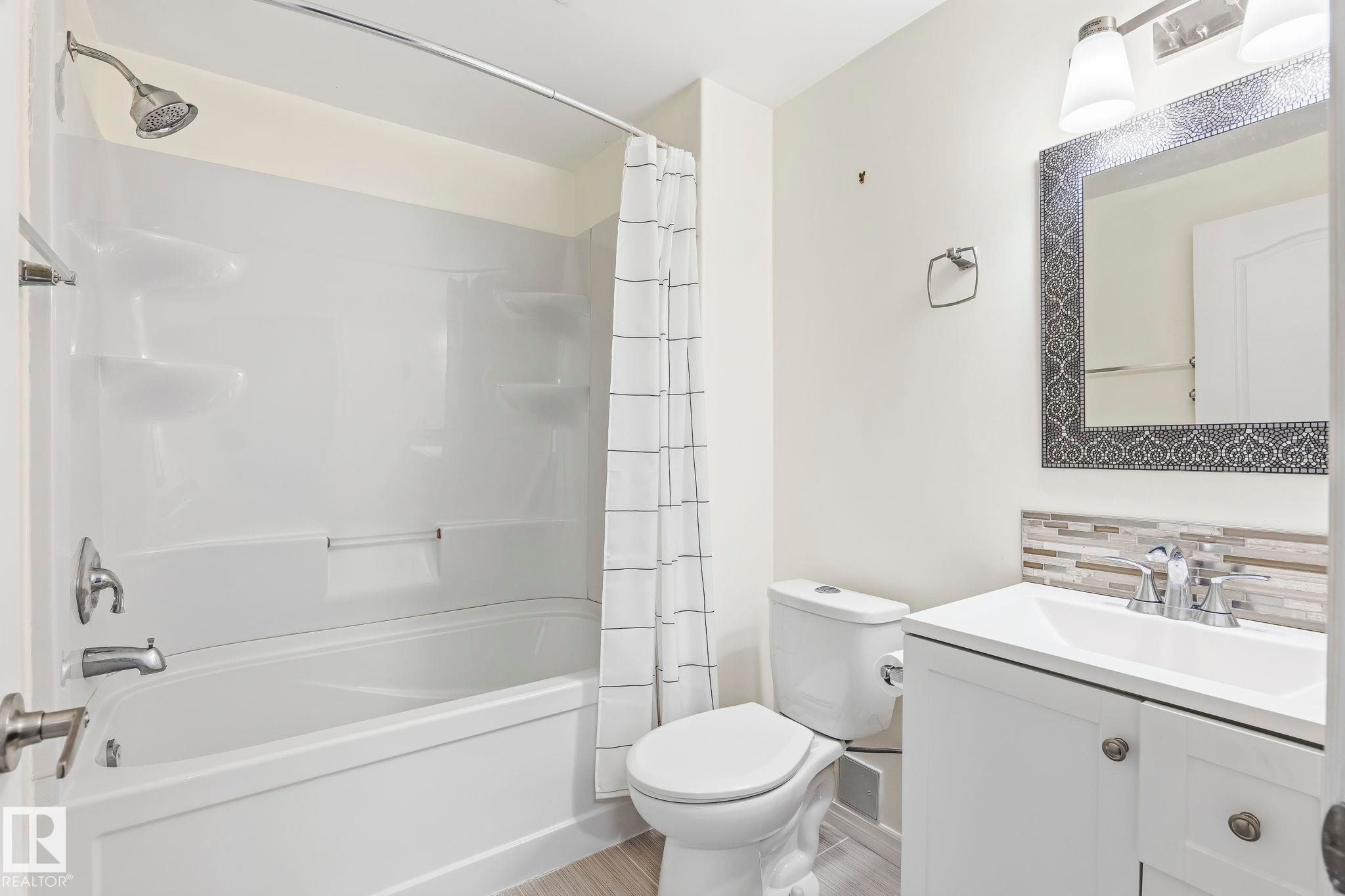 Bathroom featuring a white vanity with a rectangular sink, a patterned mirror, a white toilet, and a bathtub with an integrated shower - 4783 Crabapplle Run, Edmonton, AB - Indoor Photo Showing Bathroom