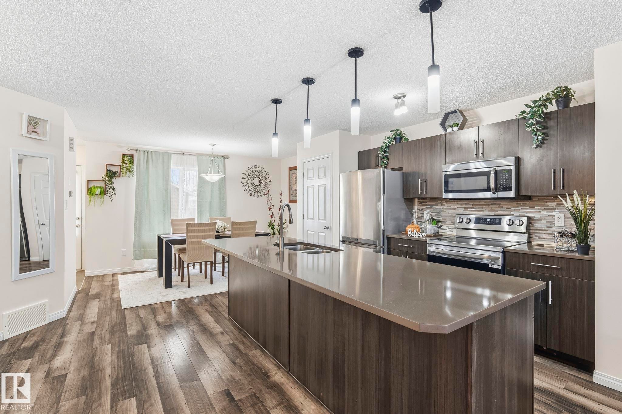 The kitchen features stainless steel appliances, dark wood cabinetry, a tiled backsplash, and a large central island with a countertop - 4783 Crabapplle Run, Edmonton, AB - Indoor Photo Showing Kitchen With Upgraded Kitchen