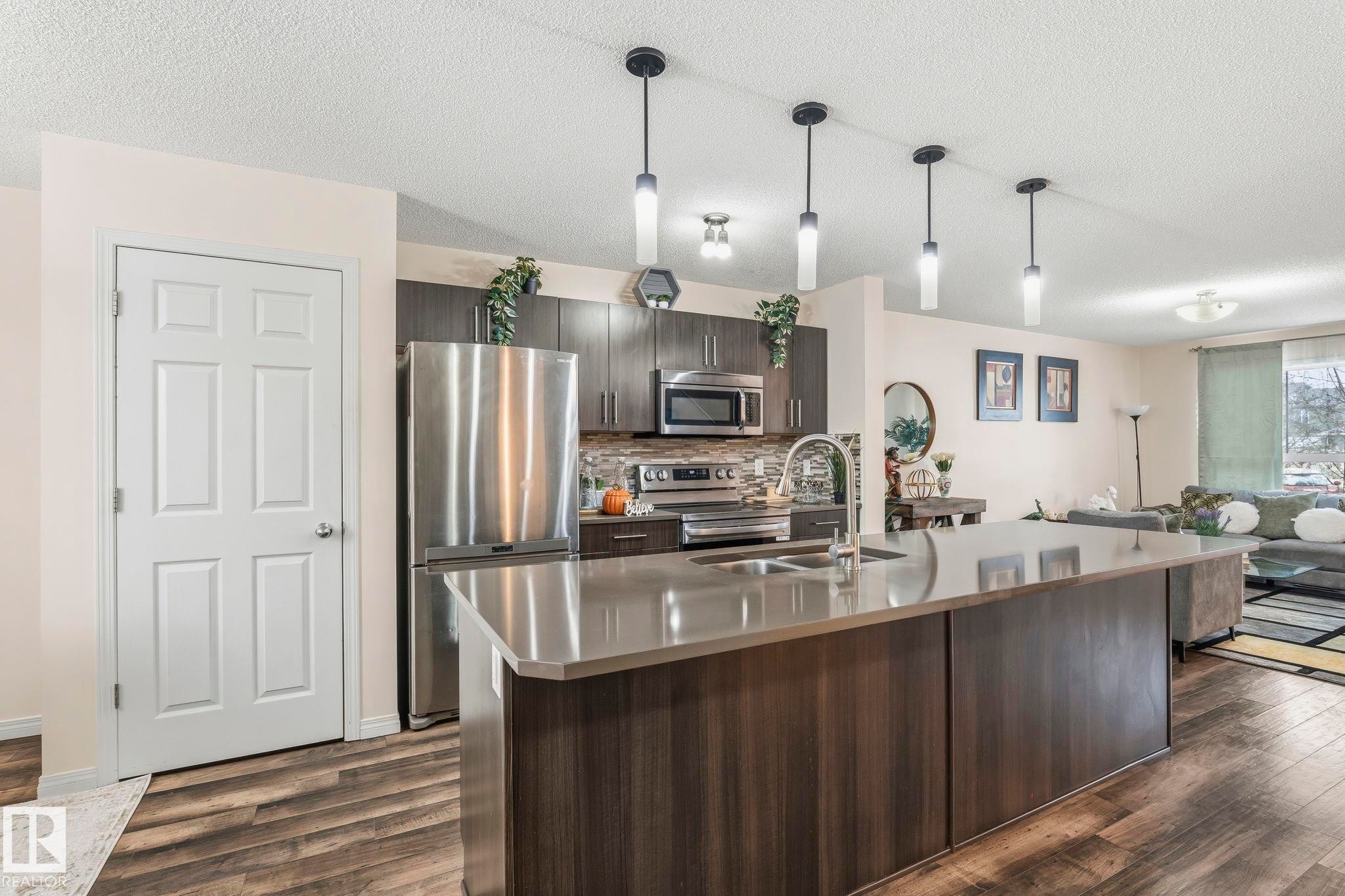 The kitchen features a large island with a sink, pendant lighting, stainless steel appliances, and dark wood cabinetry - 4783 Crabapplle Run, Edmonton, AB - Indoor Photo Showing Kitchen With Double Sink With Upgraded Kitchen