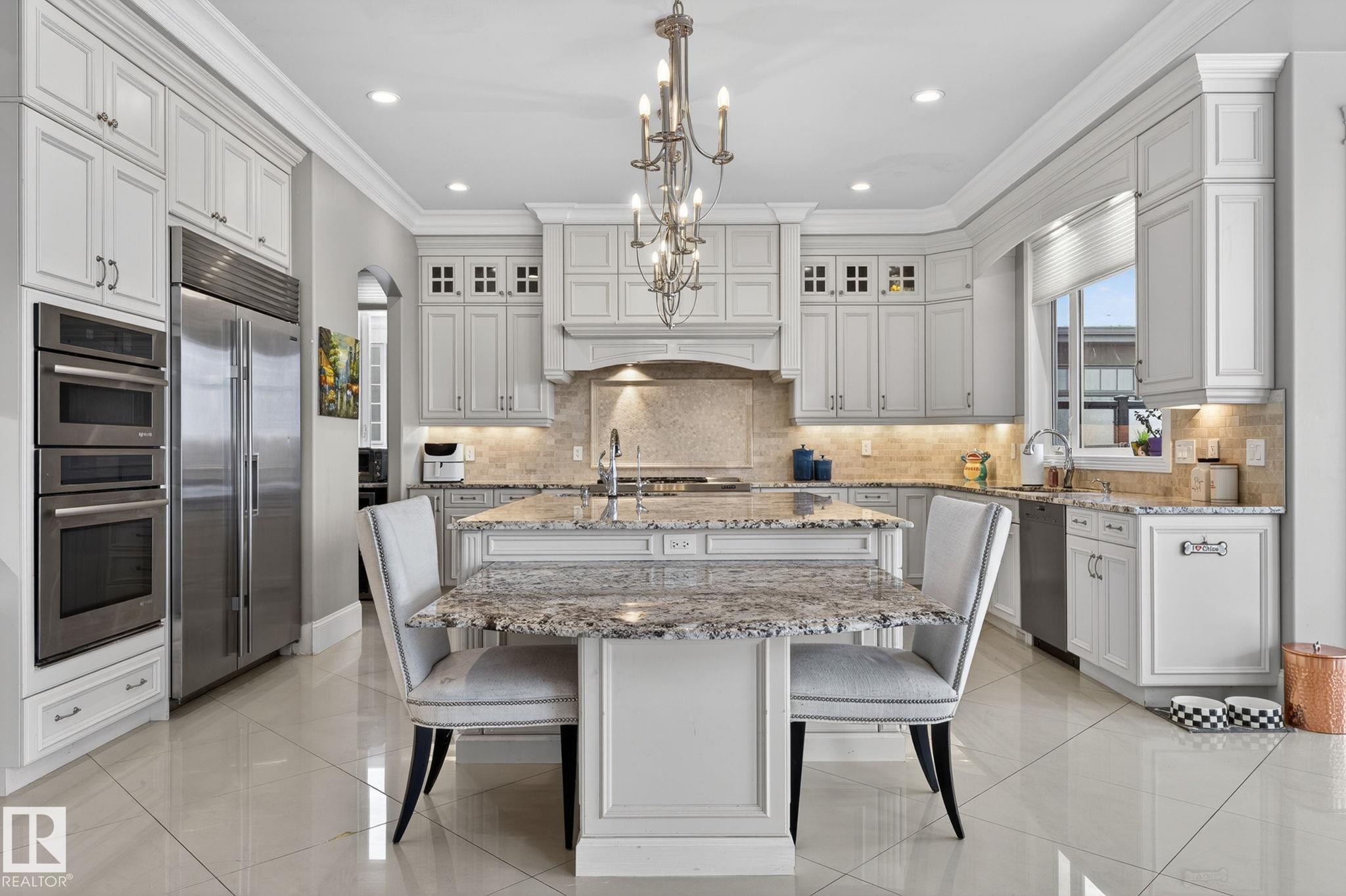 Well-appointed kitchen featuring a large central island with a granite countertop, a stainless steel refrigerator, and integrated double ovens - 1413 Woodward Crescent, Edmonton, AB - Indoor Photo Showing Kitchen With Upgraded Kitchen