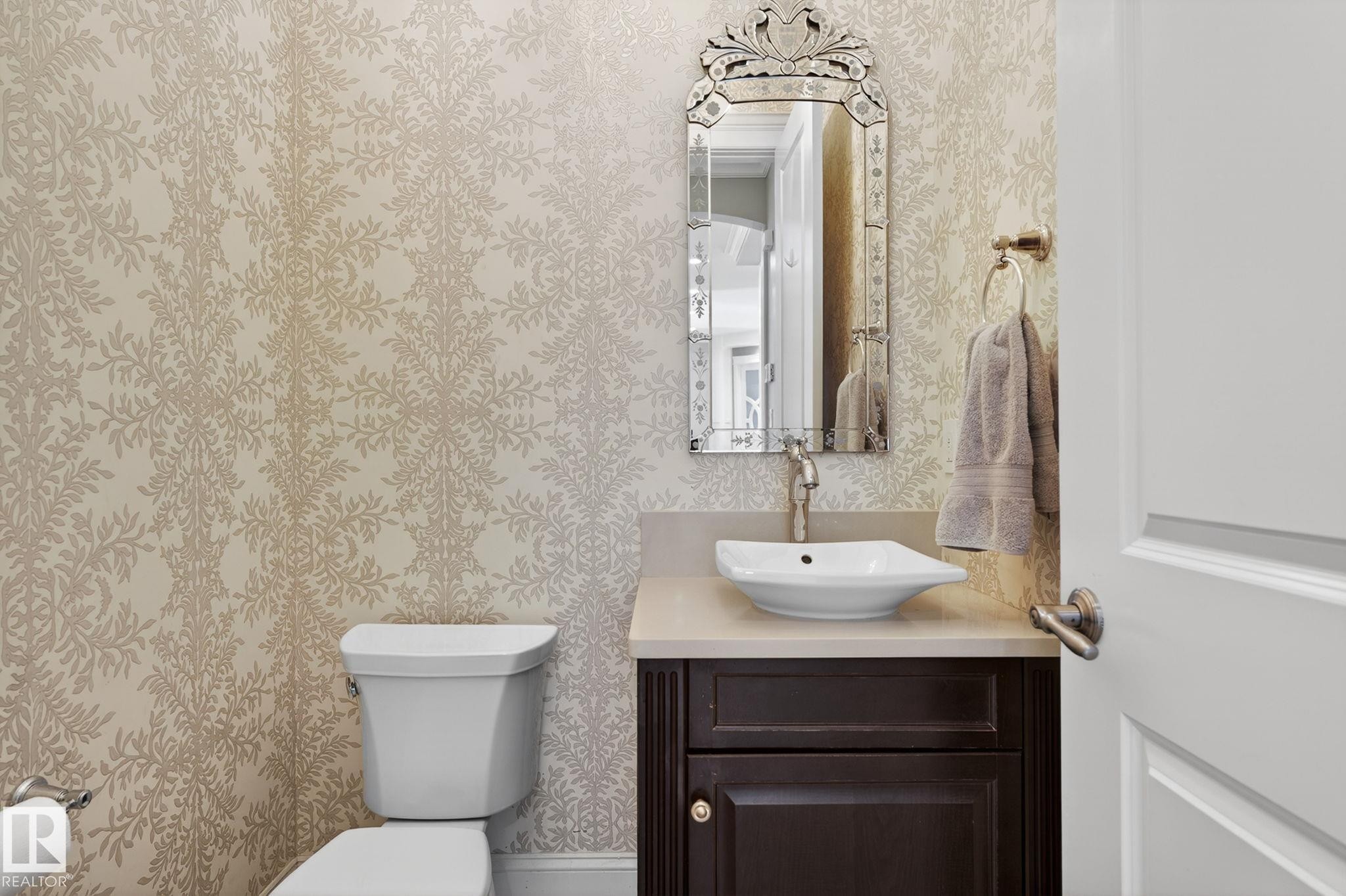 This well-appointed powder room features a sophisticated patterned wallpaper, a dark wood vanity with a light-colored countertop, and a decorative mirror above the vessel sink - 1413 Woodward Crescent, Edmonton, AB - Indoor Photo Showing Bathroom