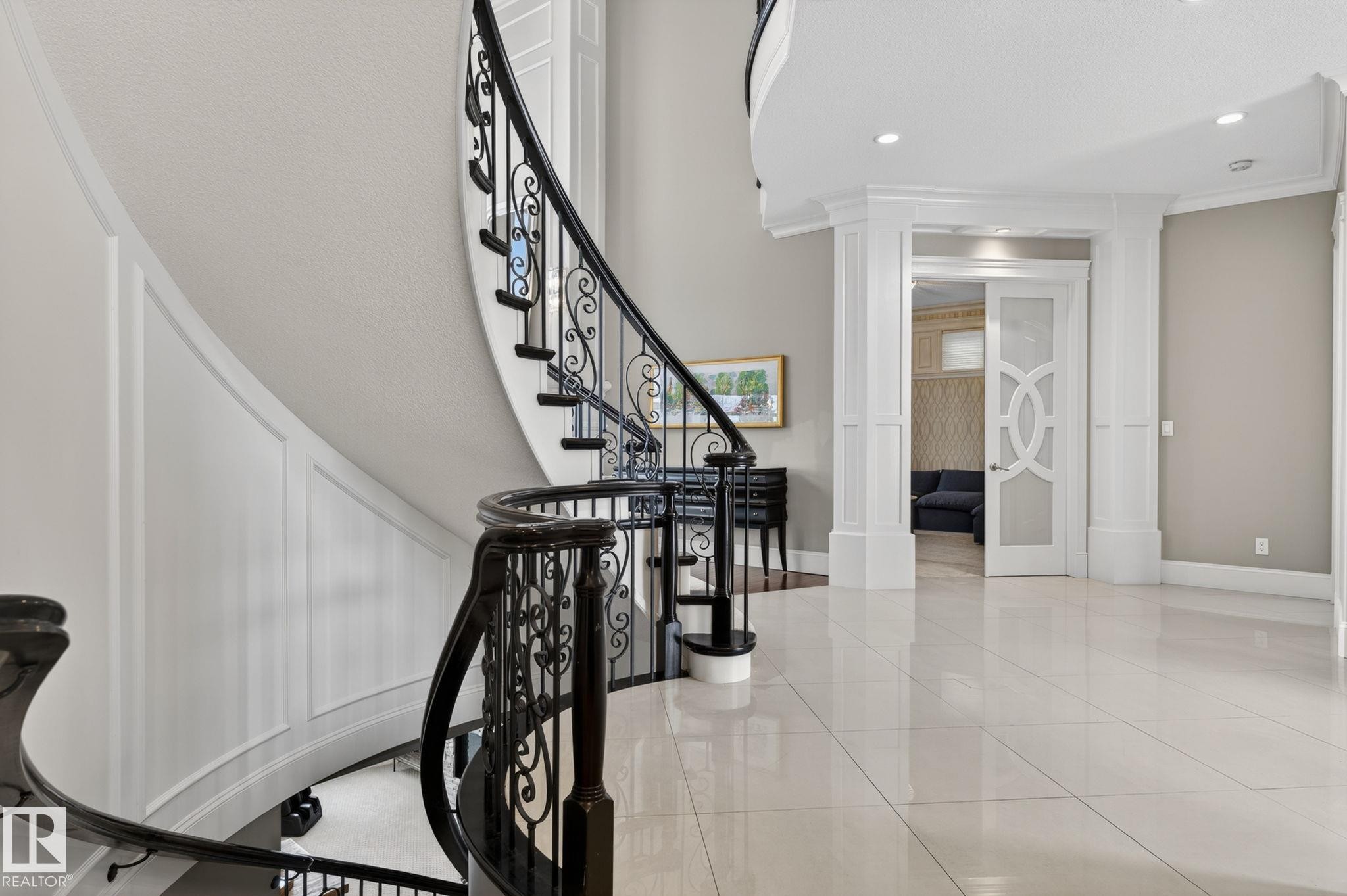This property features a grand curved staircase with ornate black wrought iron balusters and a dark wood handrail, complemented by extensive white wainscoting - 1413 Woodward Crescent, Edmonton, AB - Indoor Photo Showing Other Room