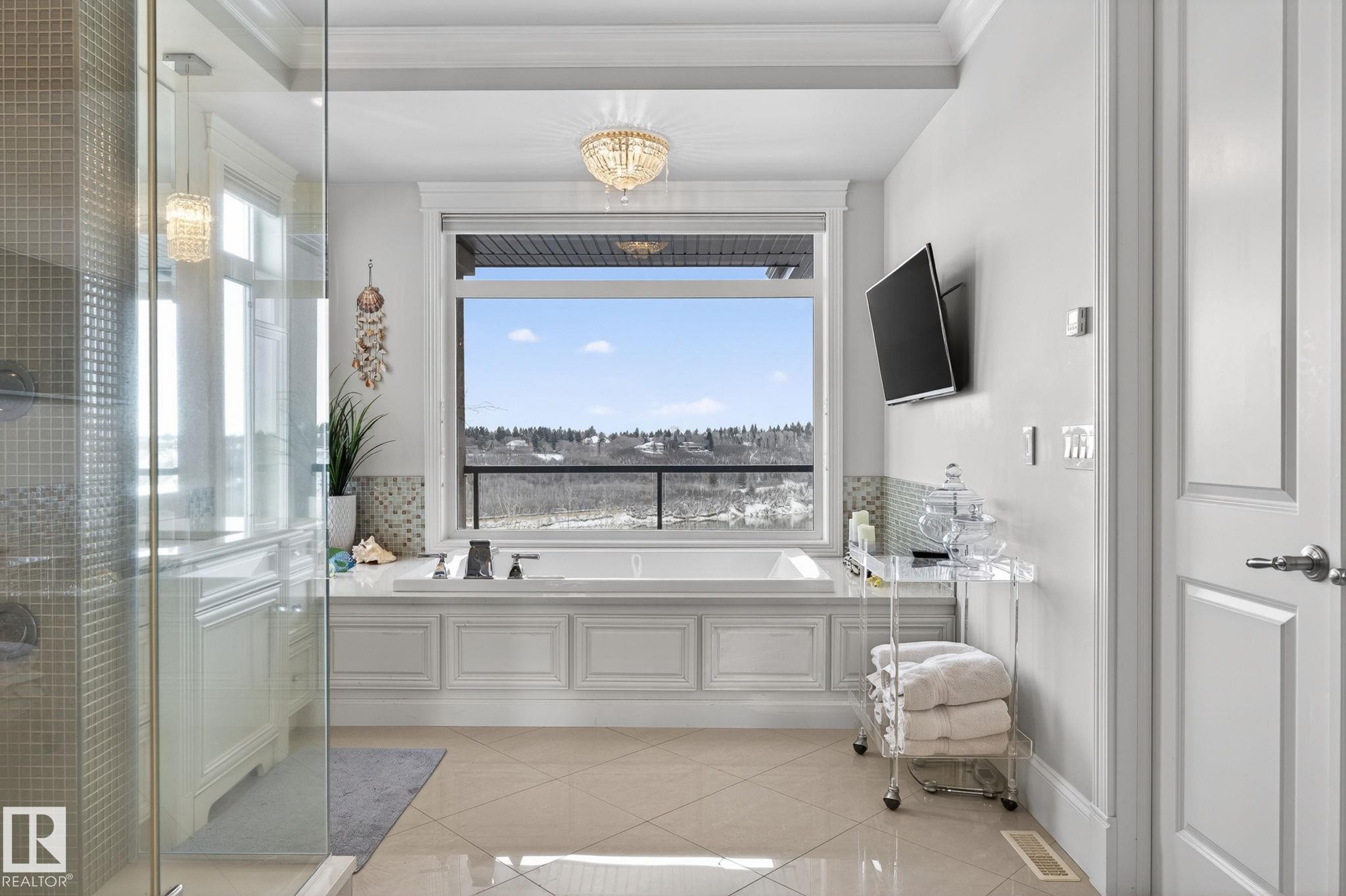 Spacious bathroom featuring a large soaking tub with a view, a glass-enclosed shower, tile flooring, and a chandelier light fixture - 1413 Woodward Crescent, Edmonton, AB - Indoor Photo Showing Bathroom