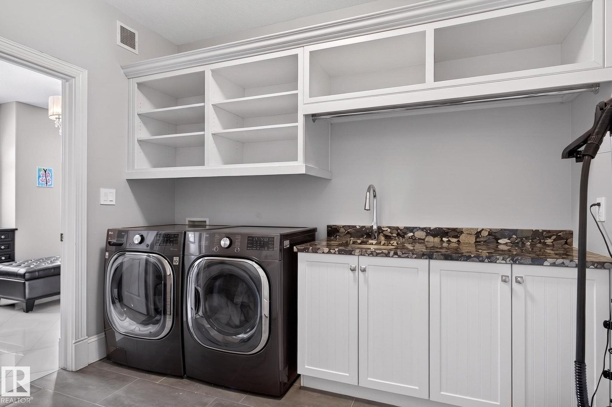 The laundry area features white cabinetry with open shelving and a hanging rod, a sink set into a patterned countertop, and dark-toned washing machines - 1413 Woodward Crescent, Edmonton, AB - Indoor Photo Showing Laundry Room