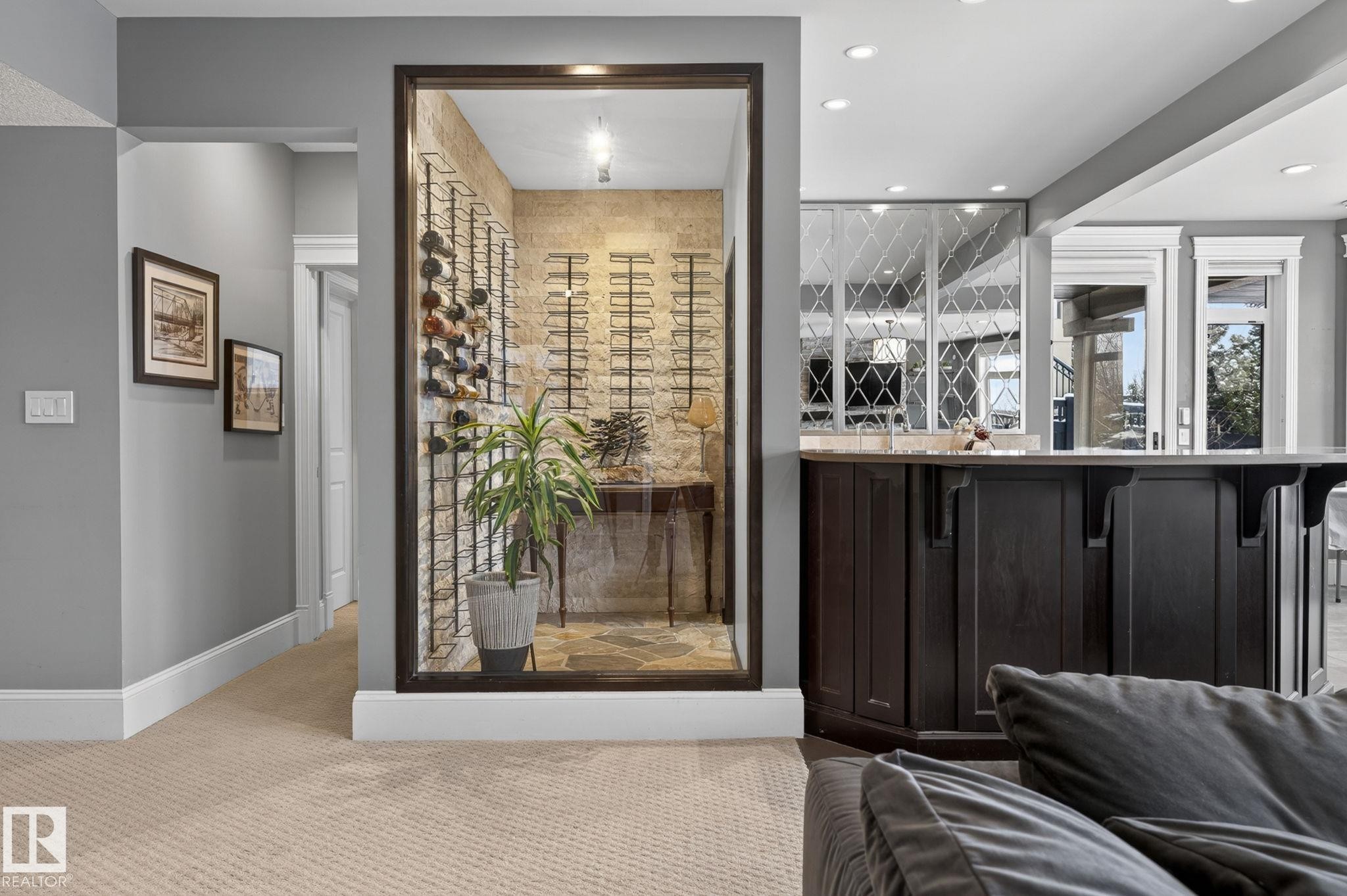 This inviting space features a custom wine cellar with stone walls and wine racks, a wet bar with dark cabinetry and a patterned mirrored backsplash, and warm carpeting - 1413 Woodward Crescent, Edmonton, AB - Indoor Photo Showing Other Room