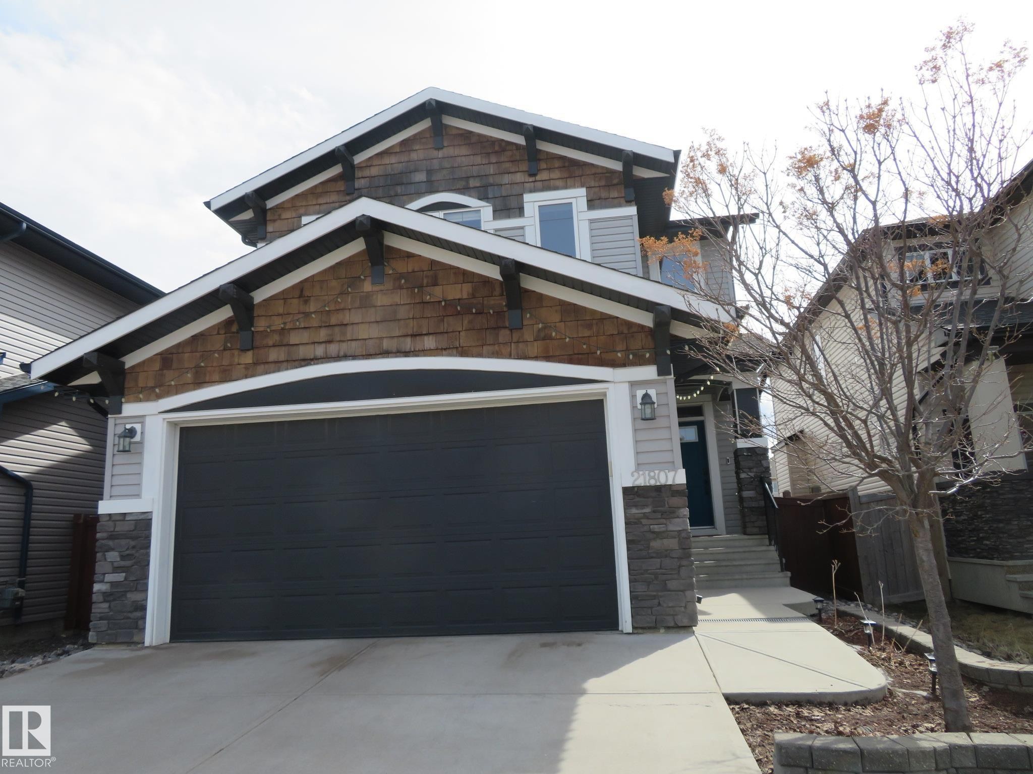 Contemporary exterior featuring wood-finish shake siding, light gray horizontal siding, and dark stone accents - 21807 97 Avenue, Edmonton, AB - Outdoor