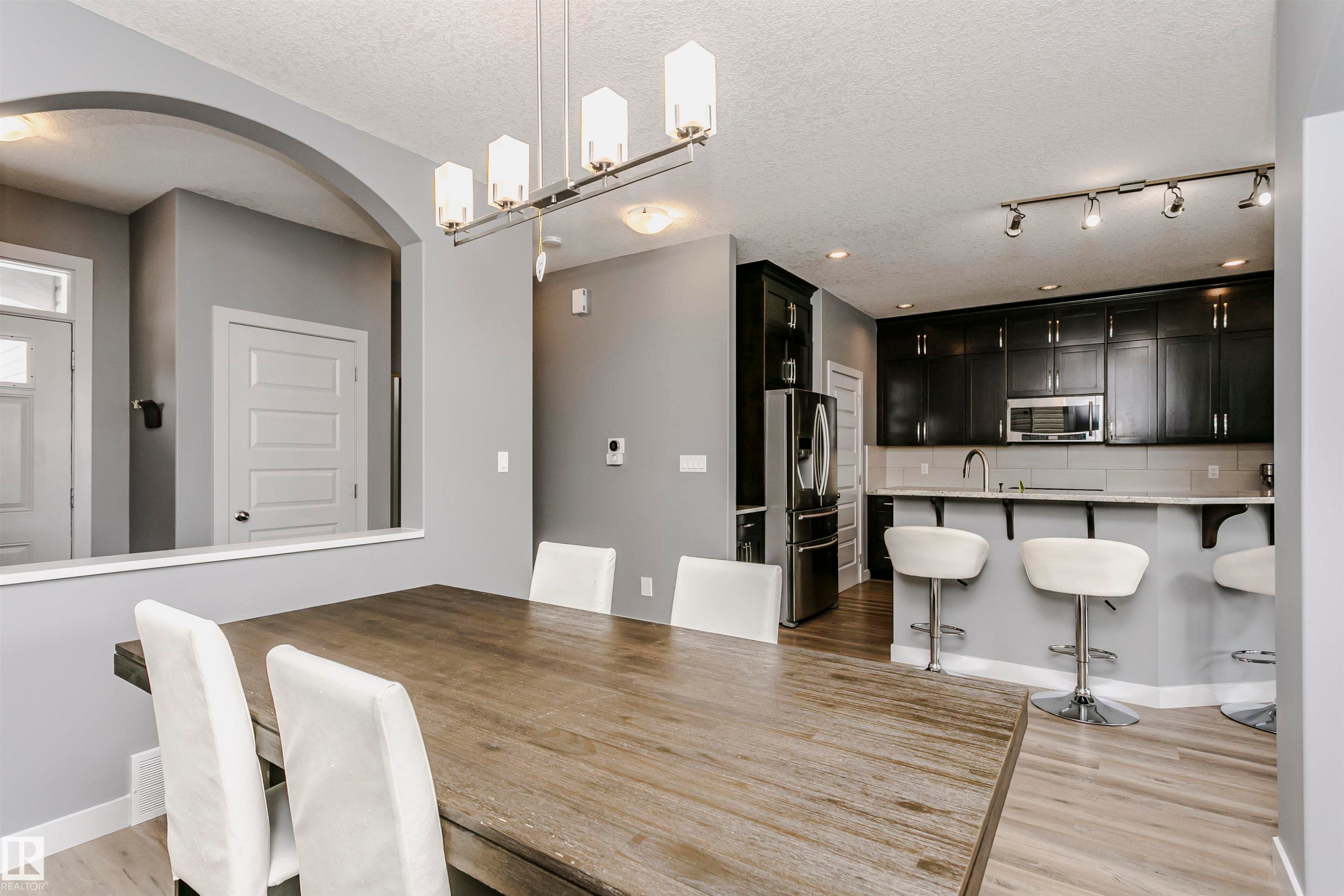 Dining area with a modern linear chandelier, an arched entryway, and light wood flooring - 21807 97 Avenue, Edmonton, AB - Indoor Photo Showing Dining Room