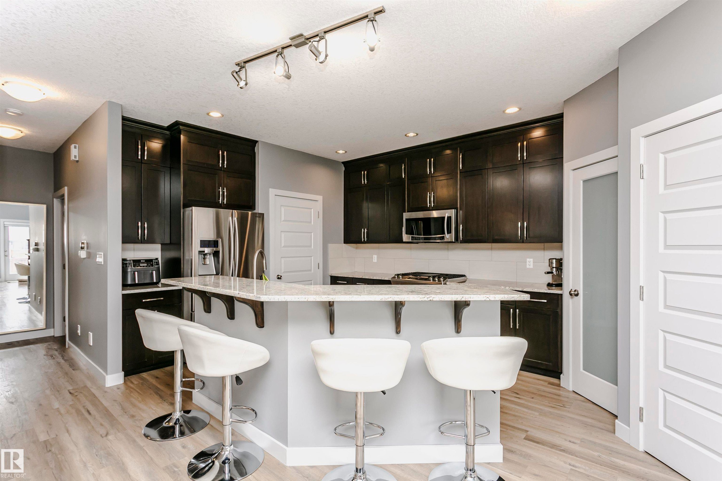 The kitchen features dark wood cabinetry, stainless steel appliances, and a light-colored countertop - 21807 97 Avenue, Edmonton, AB - Indoor Photo Showing Kitchen With Upgraded Kitchen