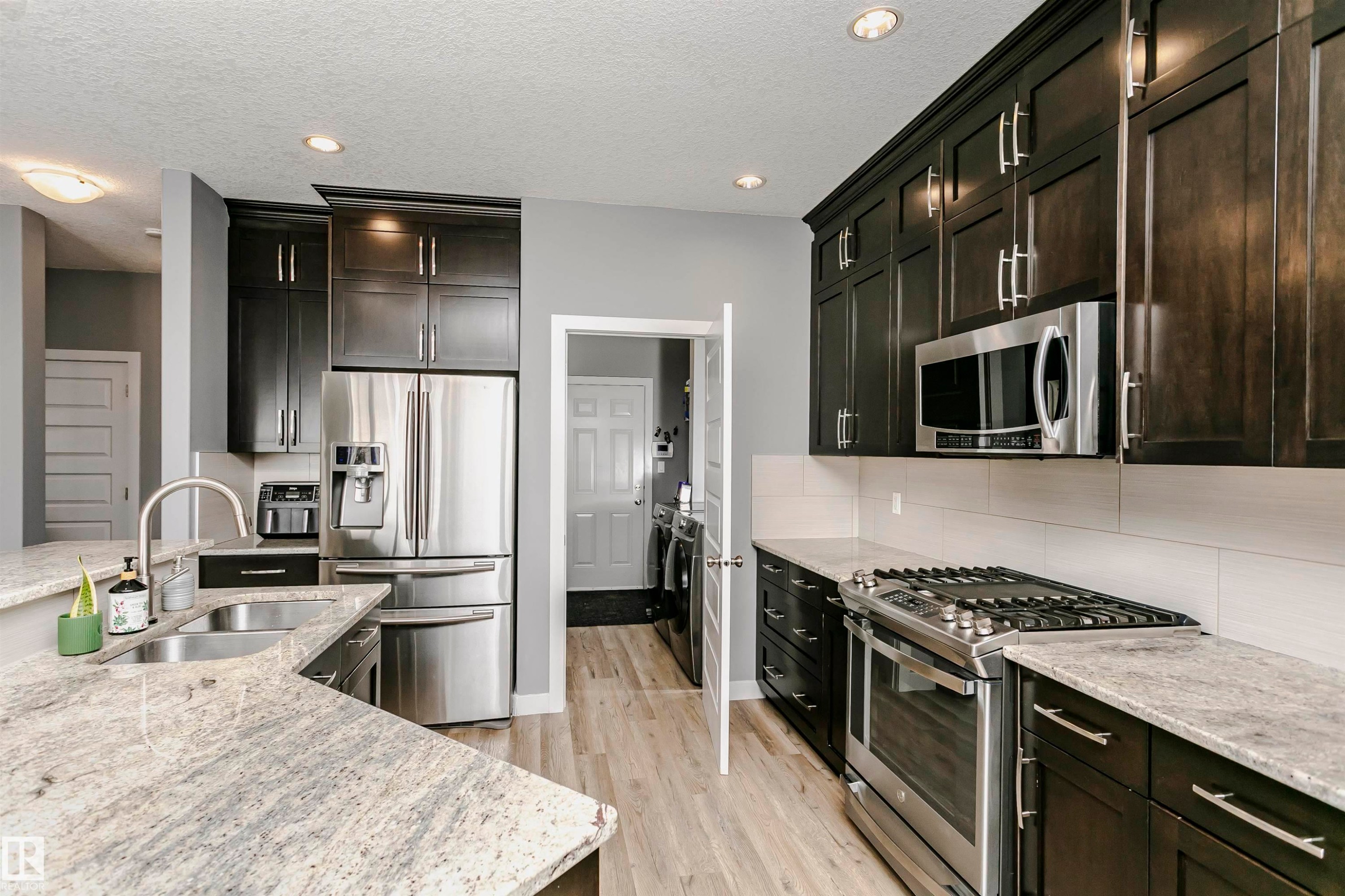 This kitchen features dark wood cabinetry, light-colored granite countertops, and stainless steel appliances, including a refrigerator, microwave, and gas range - 21807 97 Avenue, Edmonton, AB - Indoor Photo Showing Kitchen With Double Sink With Upgraded Kitchen