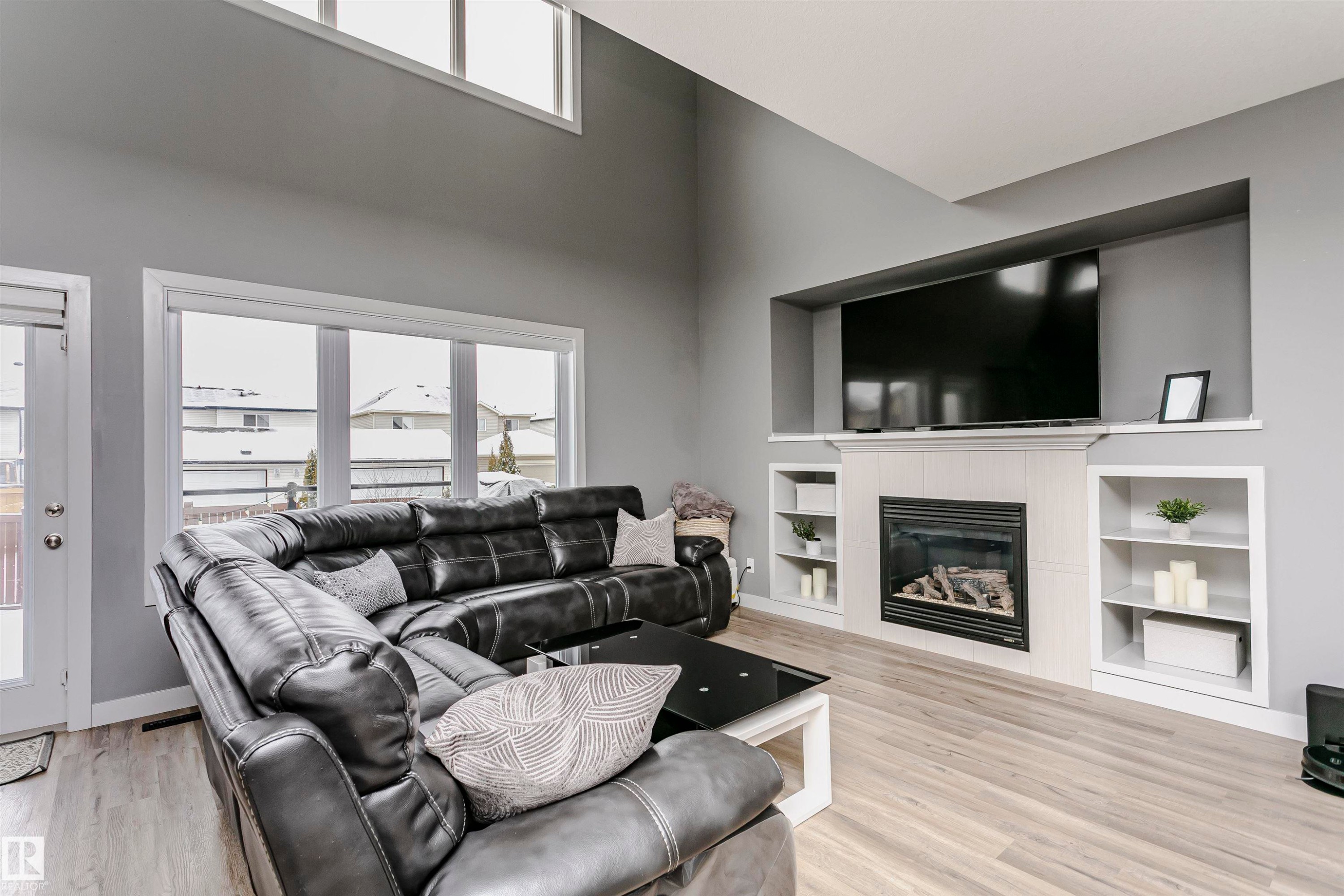 Living area featuring light wood flooring, a fireplace with a light-colored tile surround, and built-in shelving on either side - 21807 97 Avenue, Edmonton, AB - Indoor Photo Showing Living Room With Fireplace