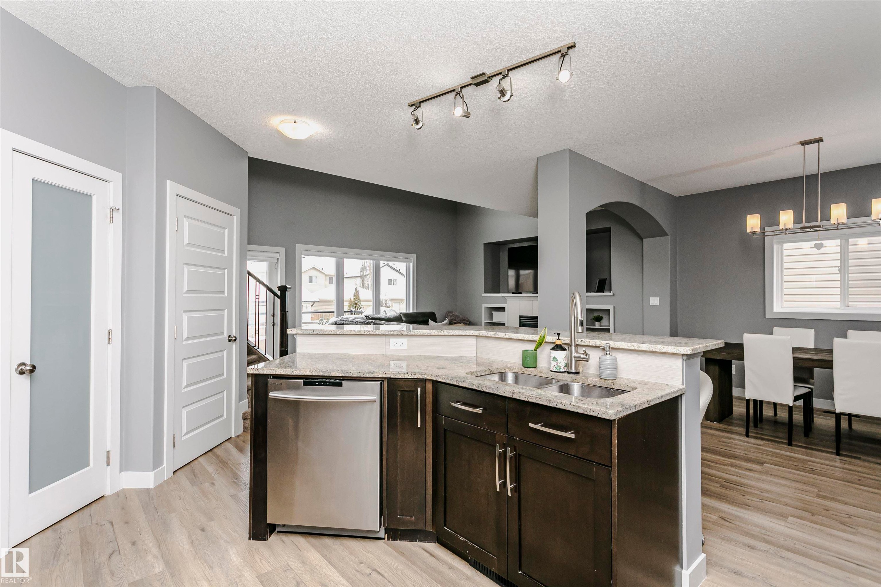 The kitchen features dark wood cabinetry, a double basin stainless steel sink, and a stainless steel dishwasher - 21807 97 Avenue, Edmonton, AB - Indoor Photo Showing Kitchen With Double Sink