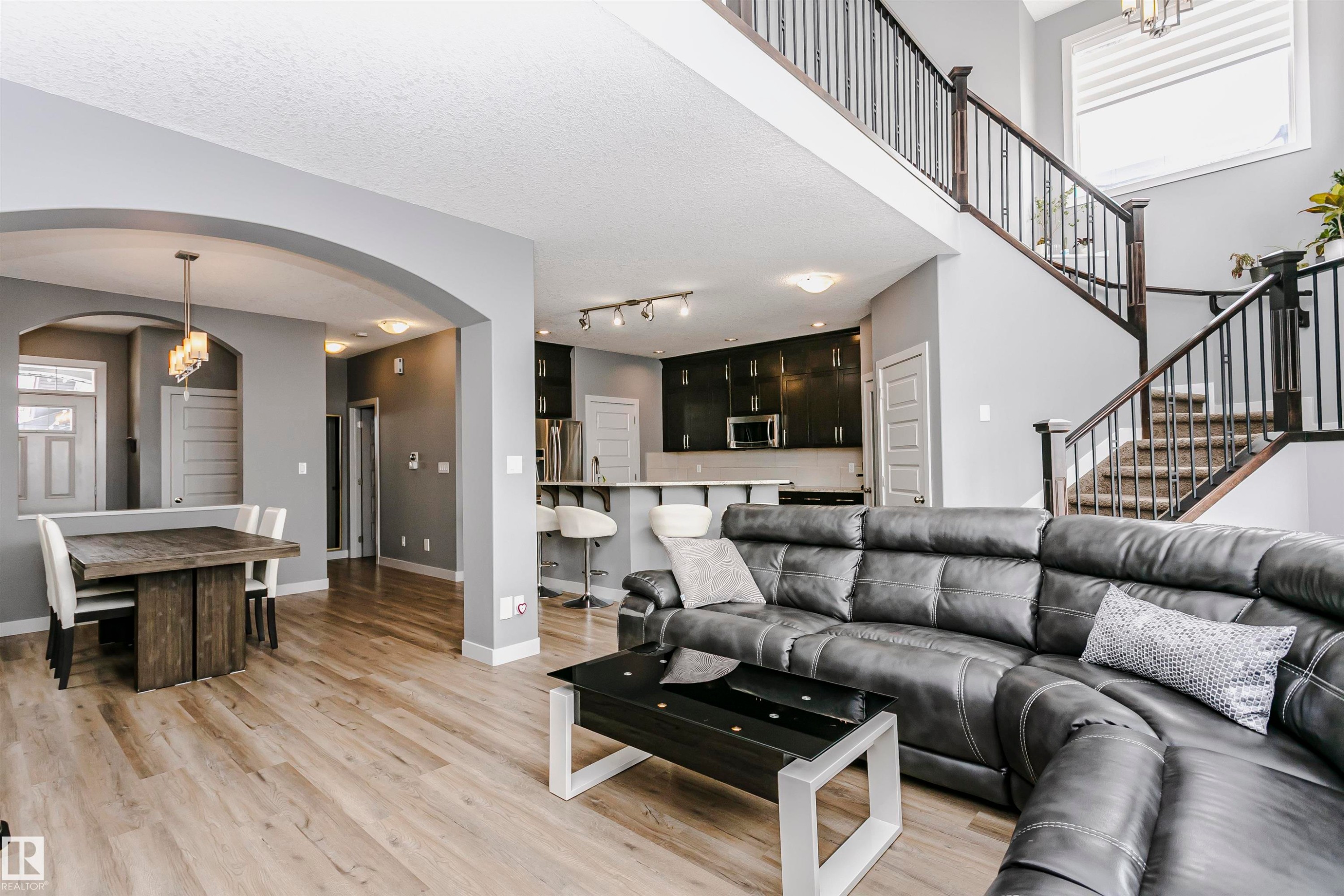 The property features an open-concept living area with light wood-style flooring, a dining area with an arched entryway, and a kitchen with dark cabinetry and stainless steel appliances - 21807 97 Avenue, Edmonton, AB - Indoor Photo Showing Living Room