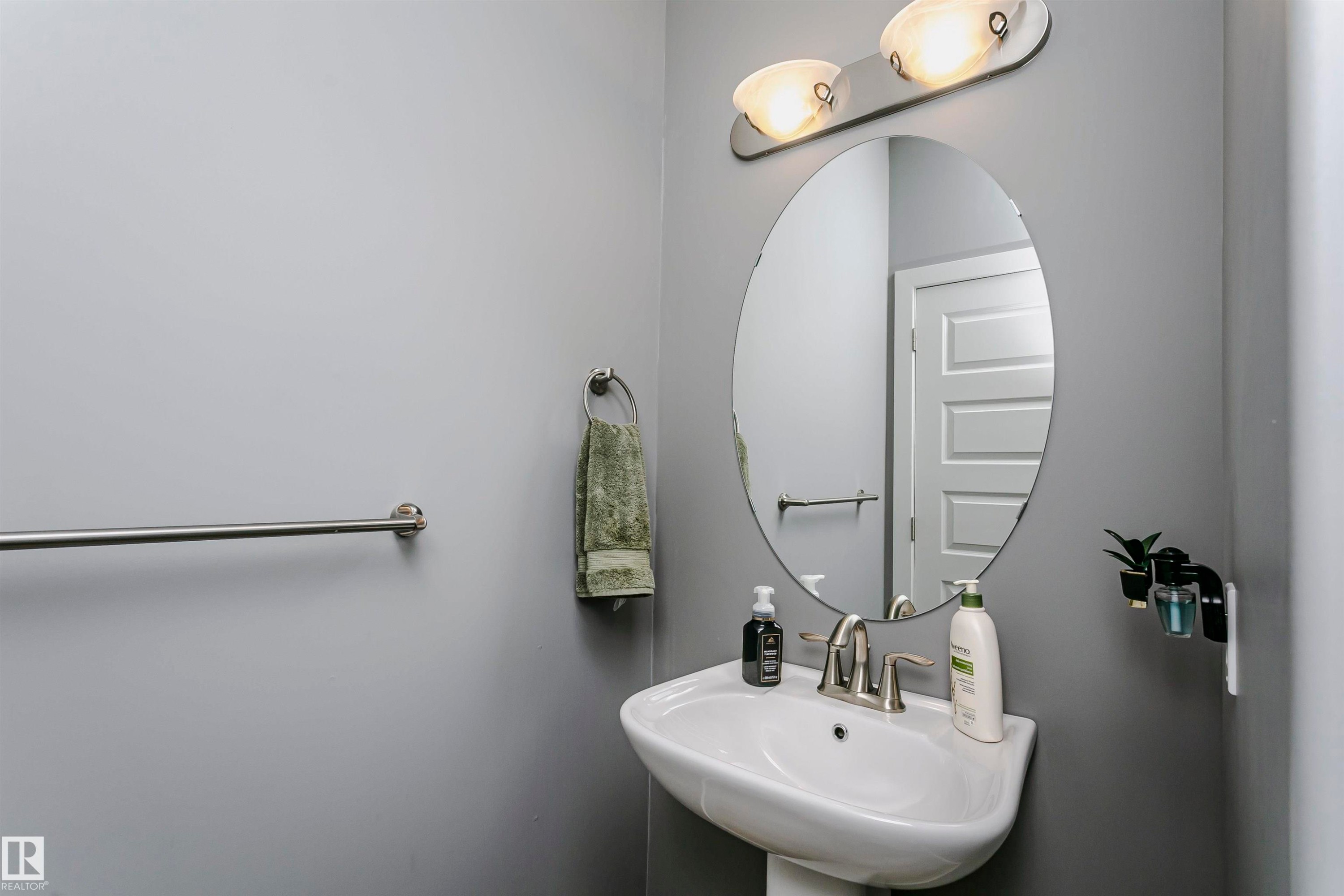 Bathroom featuring a pedestal sink, an oval mirror, and a wall-mounted light fixture with two sconces - 21807 97 Avenue, Edmonton, AB - Indoor Photo Showing Bathroom