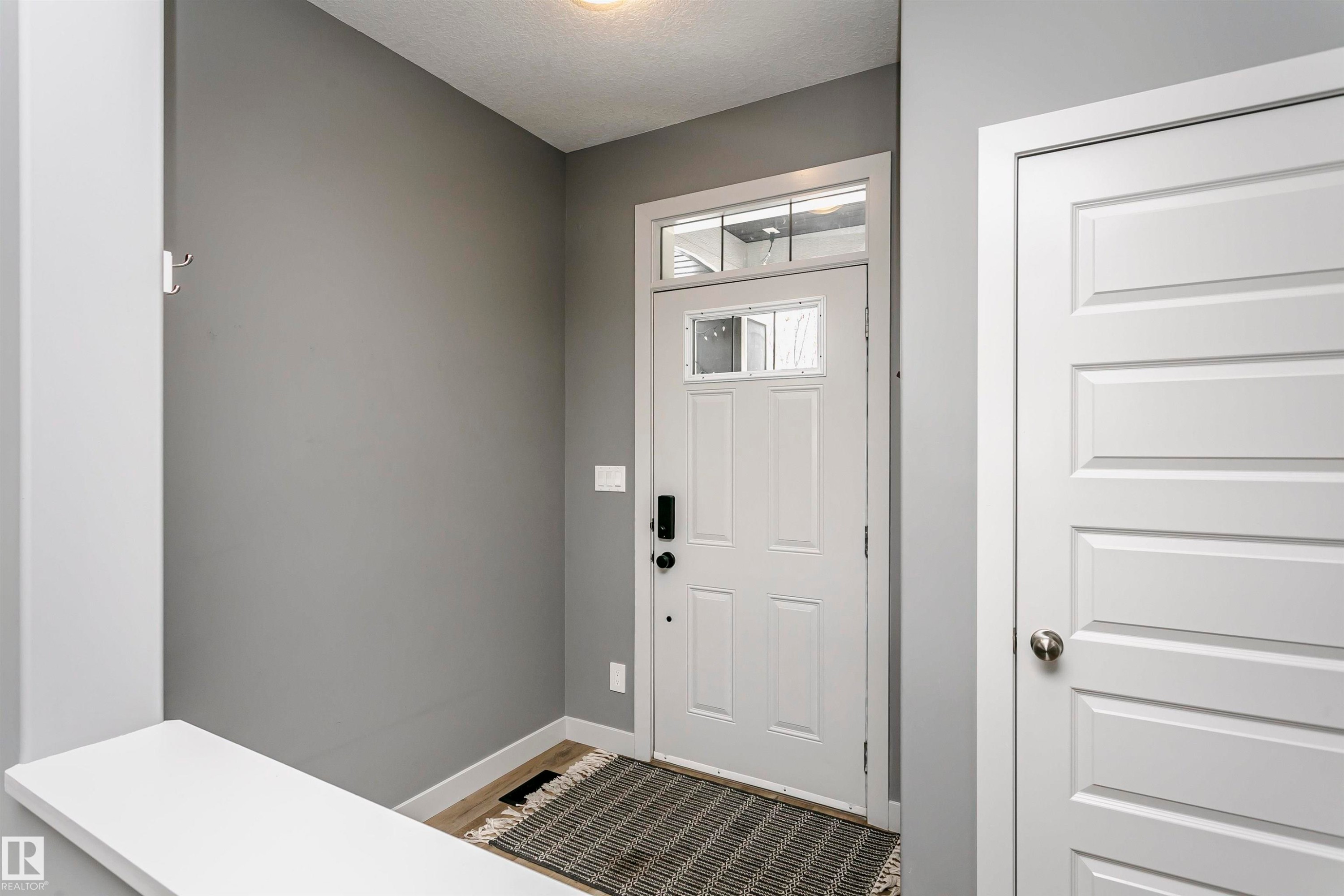 Inviting entry with a white paneled door featuring a window insert and transom window, complemented by light wood-style flooring and a neutral wall color - 21807 97 Avenue, Edmonton, AB - Indoor Photo Showing Other Room
