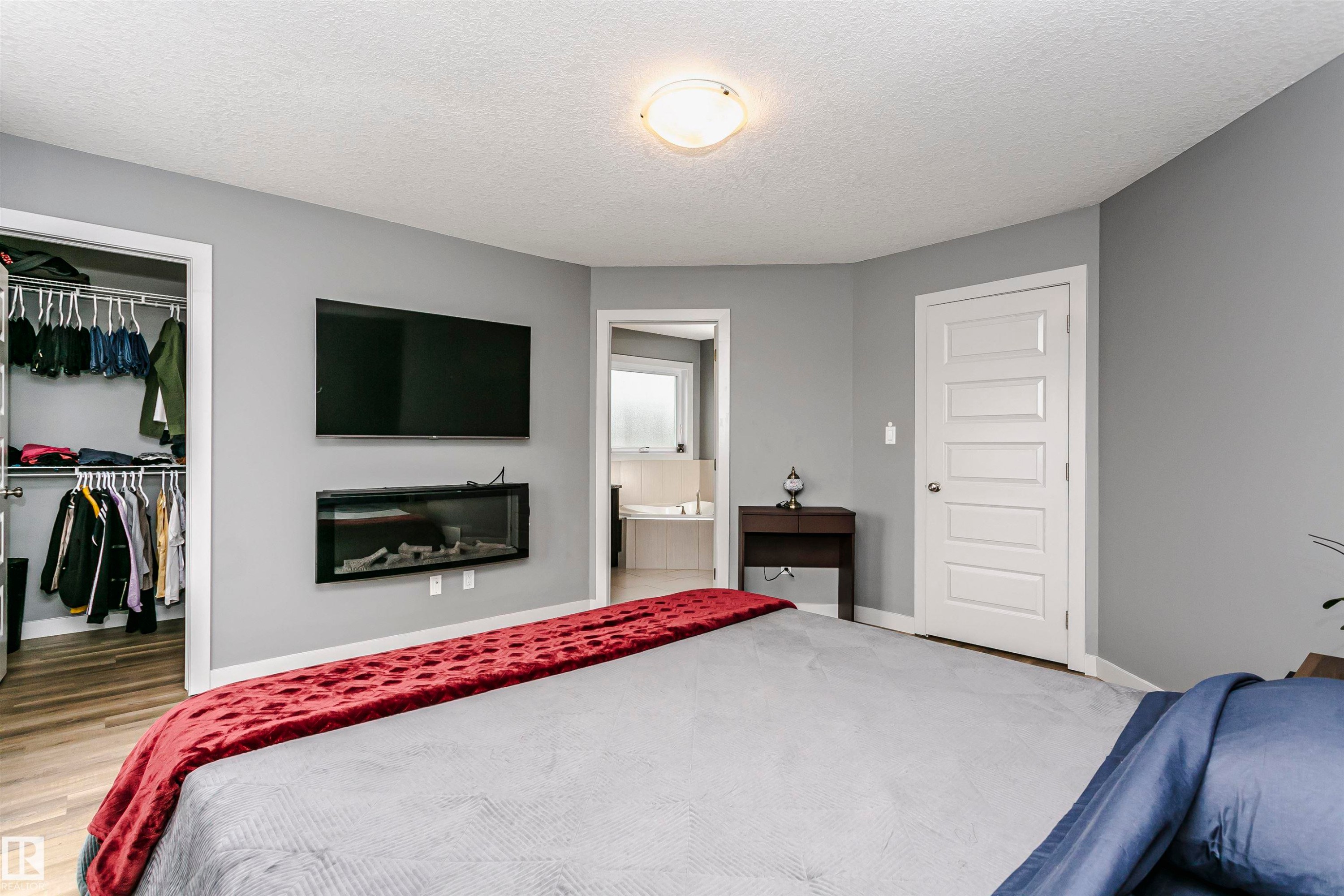 This room features a wall-mounted fireplace below a television, a walk-in closet with hanging rails, and a white paneled door - 21807 97 Avenue, Edmonton, AB - Indoor Photo Showing Bedroom