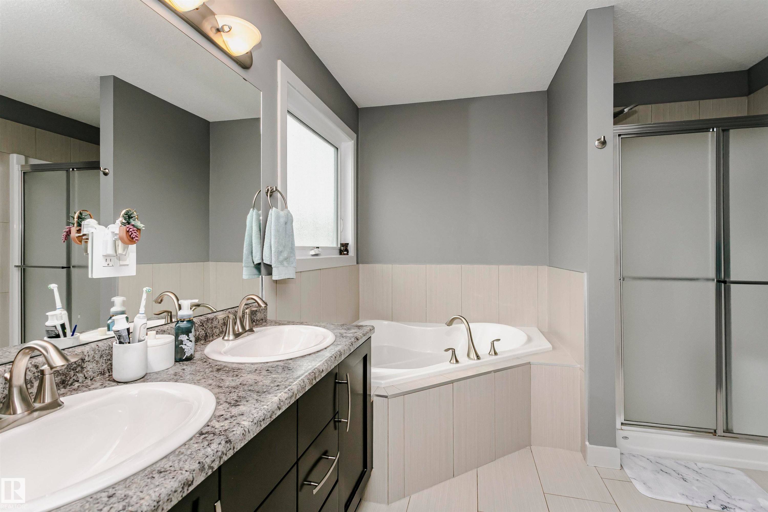 The bathroom features a double vanity with two sinks, a built-in bathtub, and a separate shower with frosted glass doors - 21807 97 Avenue, Edmonton, AB - Indoor Photo Showing Bathroom