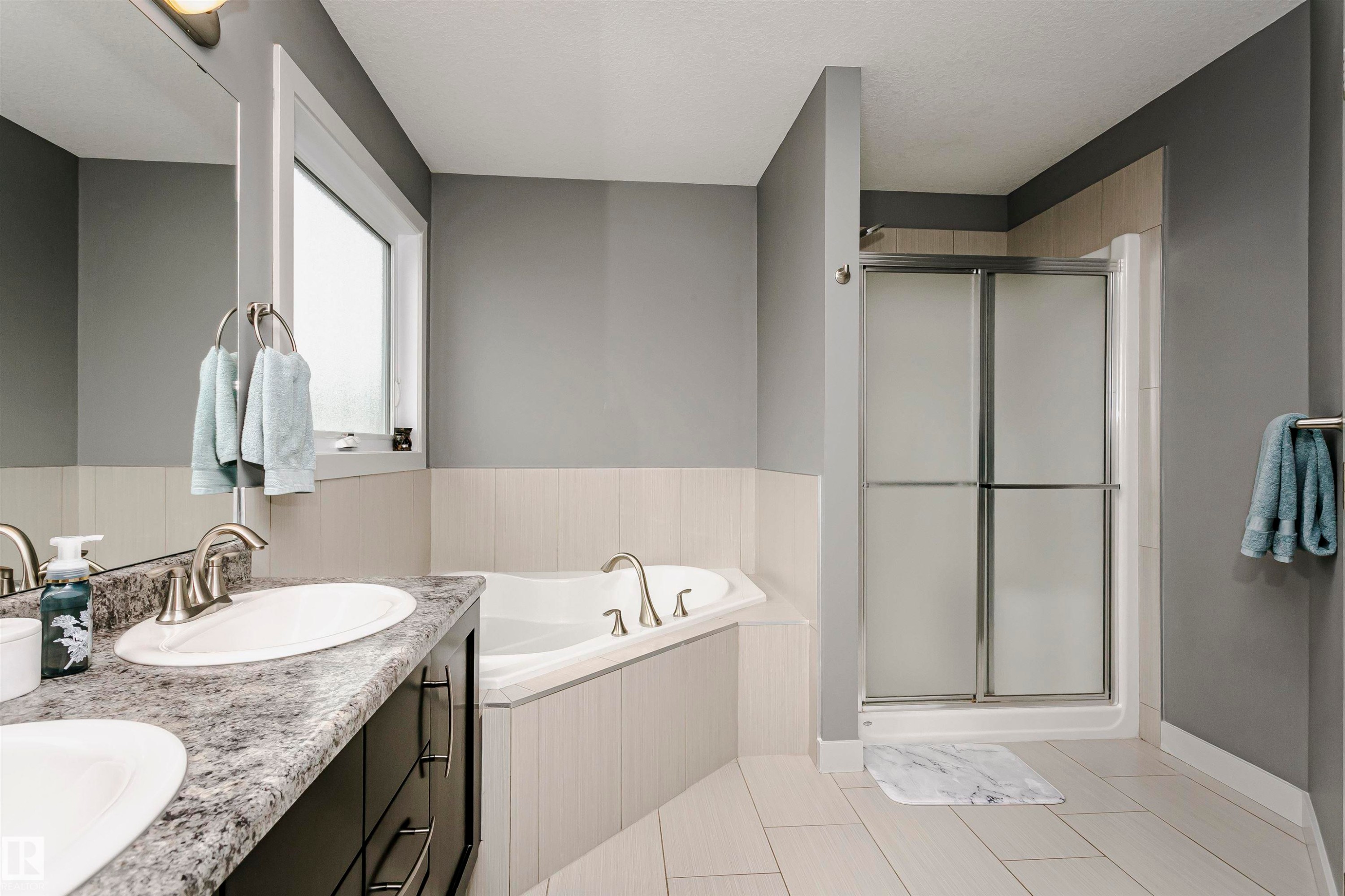 Bathroom with dual sinks, a vanity with dark cabinetry and speckled countertops, a corner soaking tub, and a shower with frosted glass doors - 21807 97 Avenue, Edmonton, AB - Indoor Photo Showing Bathroom