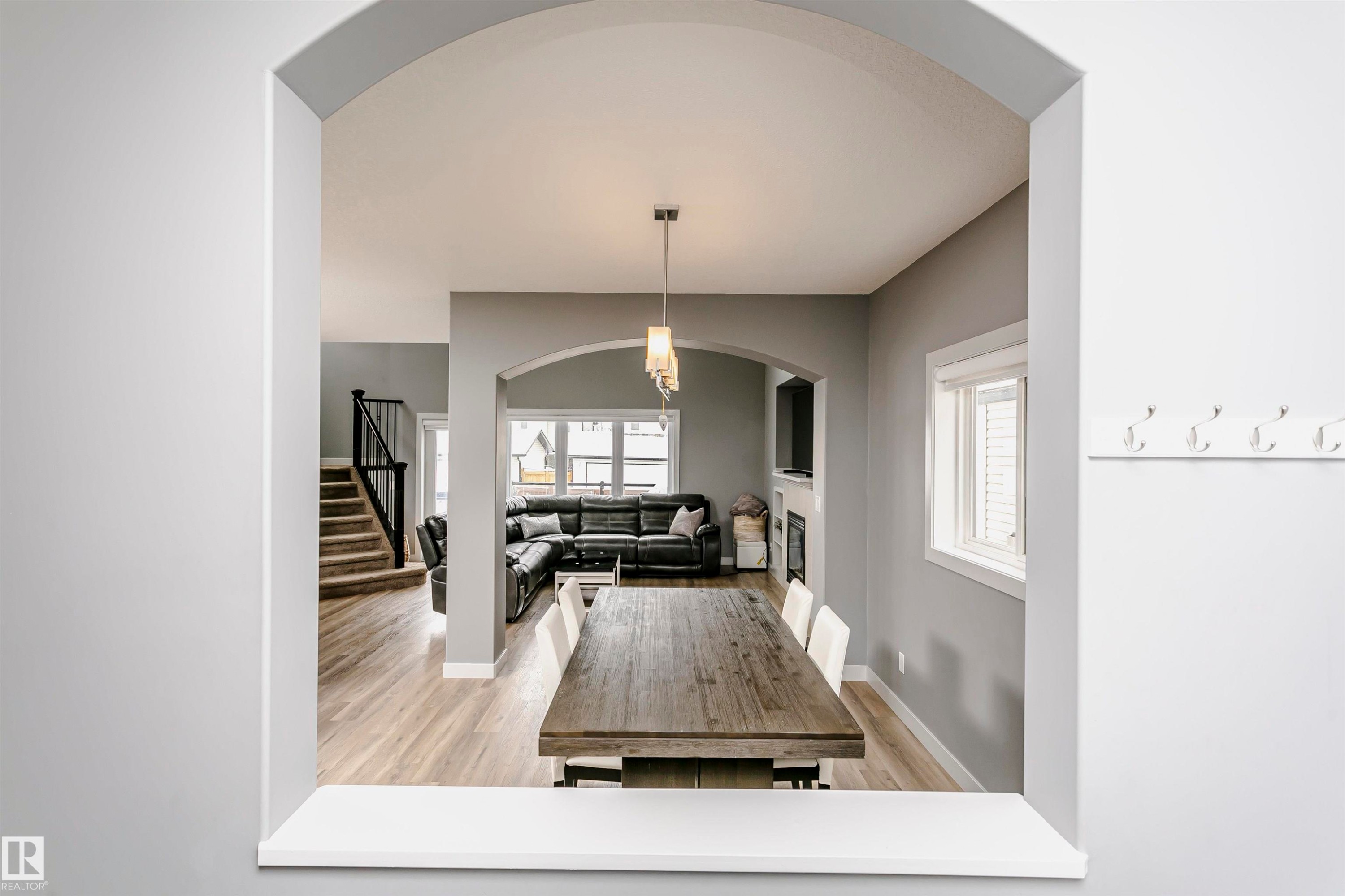 View through an arched entryway into a dining area with a wooden table and a living space featuring a fireplace, a window, and wood-style flooring - 21807 97 Avenue, Edmonton, AB - Indoor