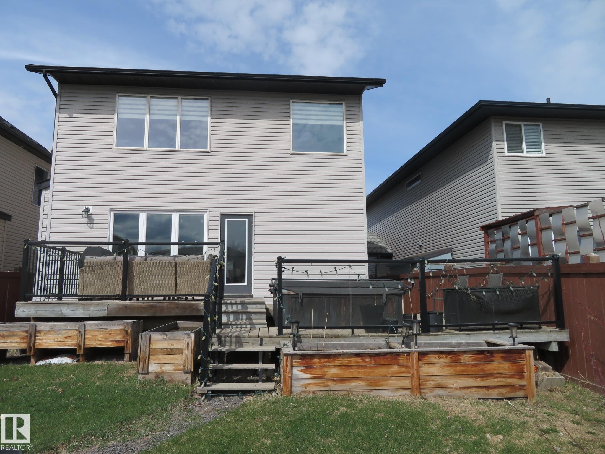 Rear exterior featuring a multi-level wood deck with black metal railings, a ground-level patio, and wood planter boxes - 21807 97 Avenue, Edmonton, AB - Outdoor With Deck Patio Veranda With Exterior