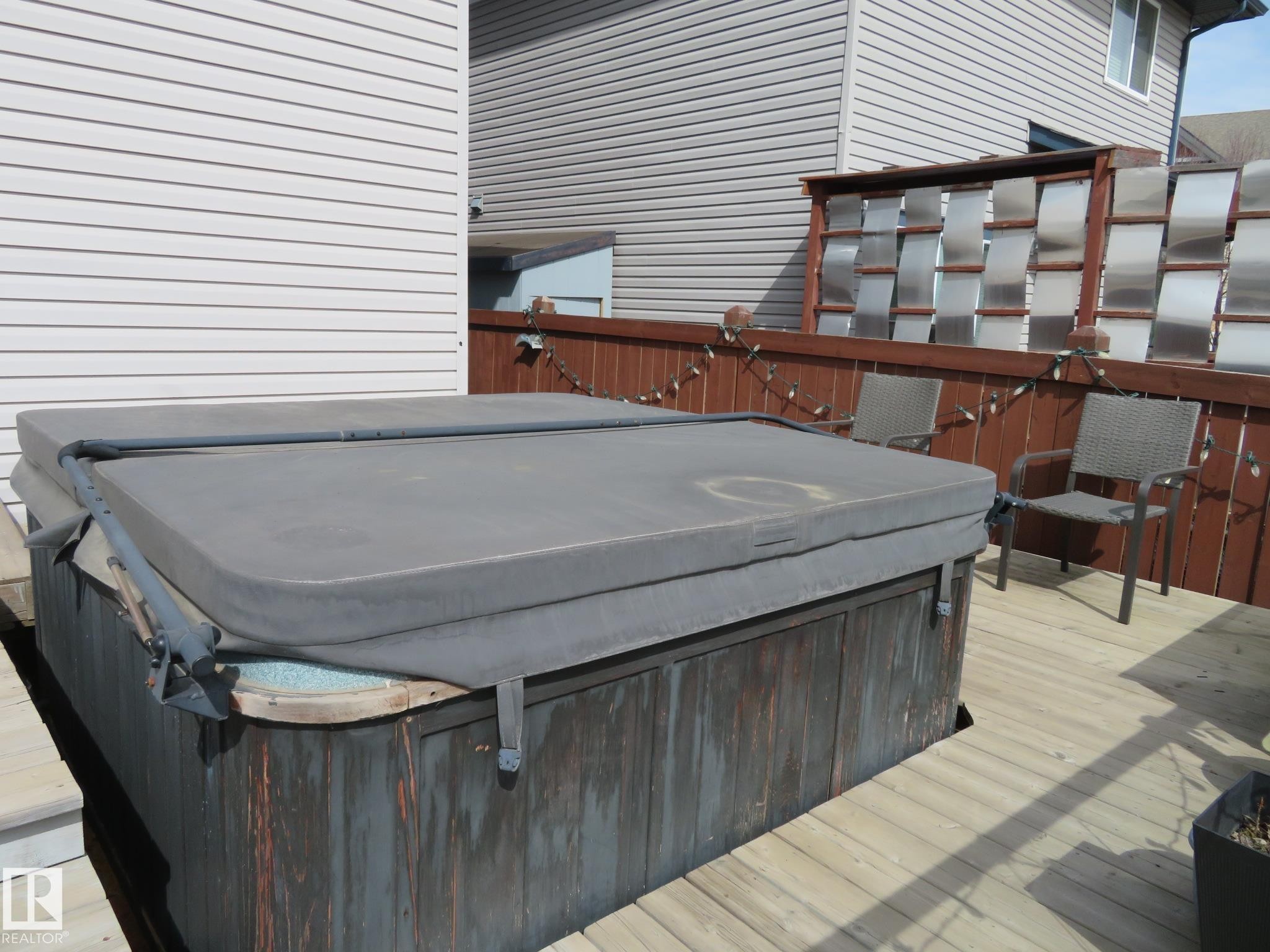 Expansive outdoor deck featuring a covered hot tub, wood privacy fencing, and an accent screen with horizontal panels - 21807 97 Avenue, Edmonton, AB - Outdoor With Exterior