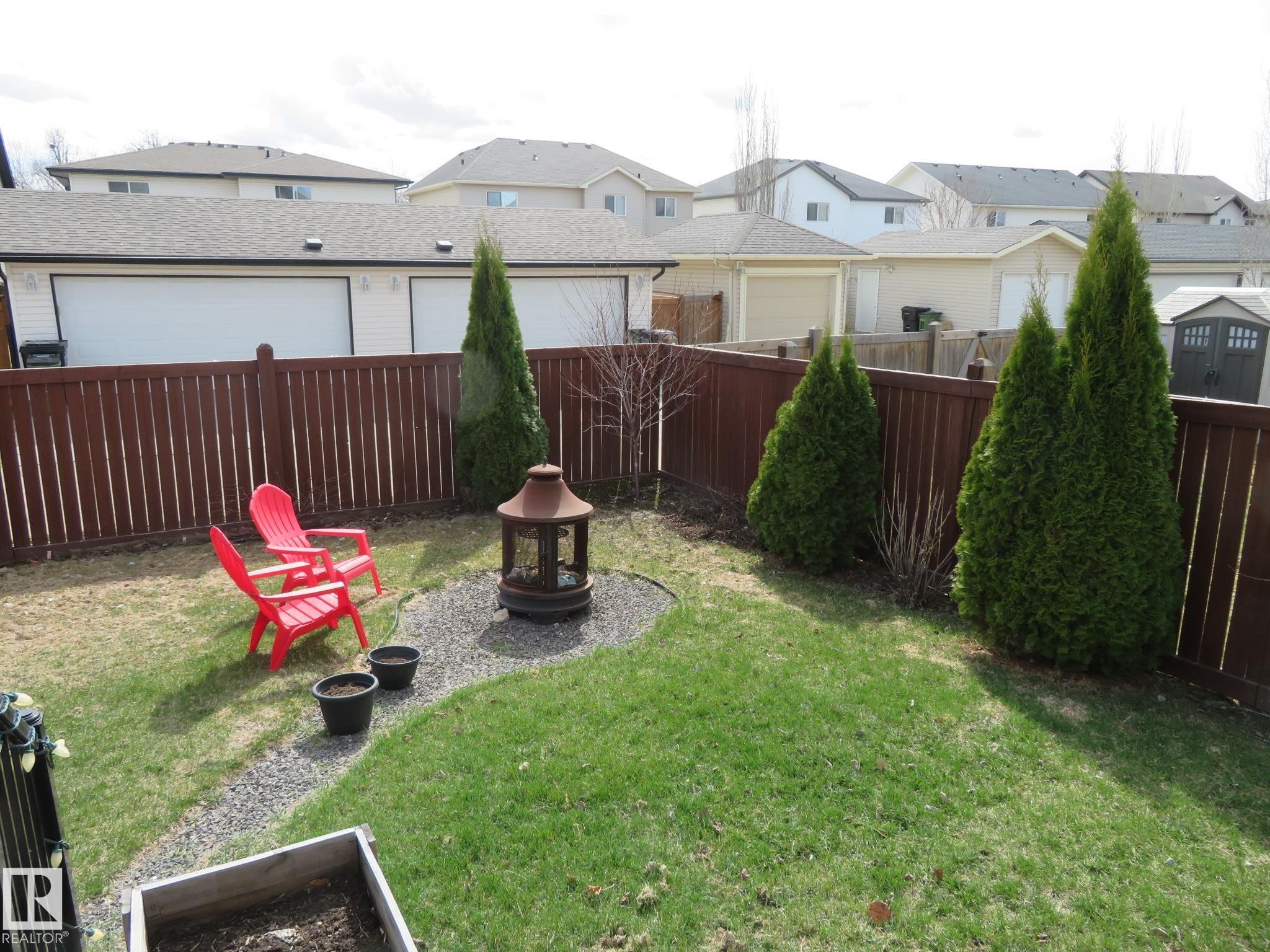 Fenced backyard featuring a gravel patio area, a fire pit, and mature evergreen shrubs - 21807 97 Avenue, Edmonton, AB - Outdoor With Deck Patio Veranda