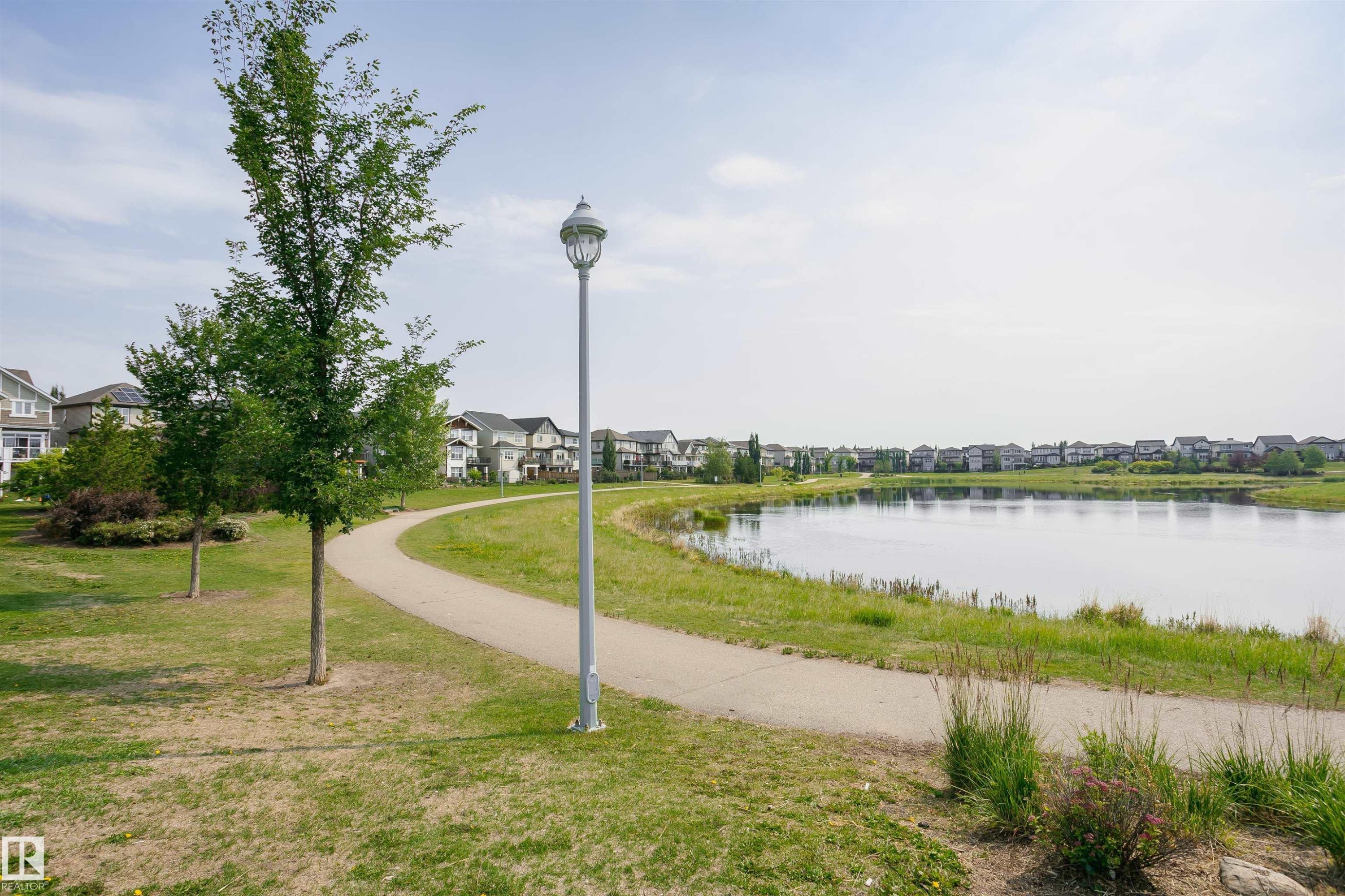 View of the community lake and surrounding residences, featuring a paved pathway and mature trees - 21807 97 Avenue, Edmonton, AB - Outdoor With Body Of Water With View