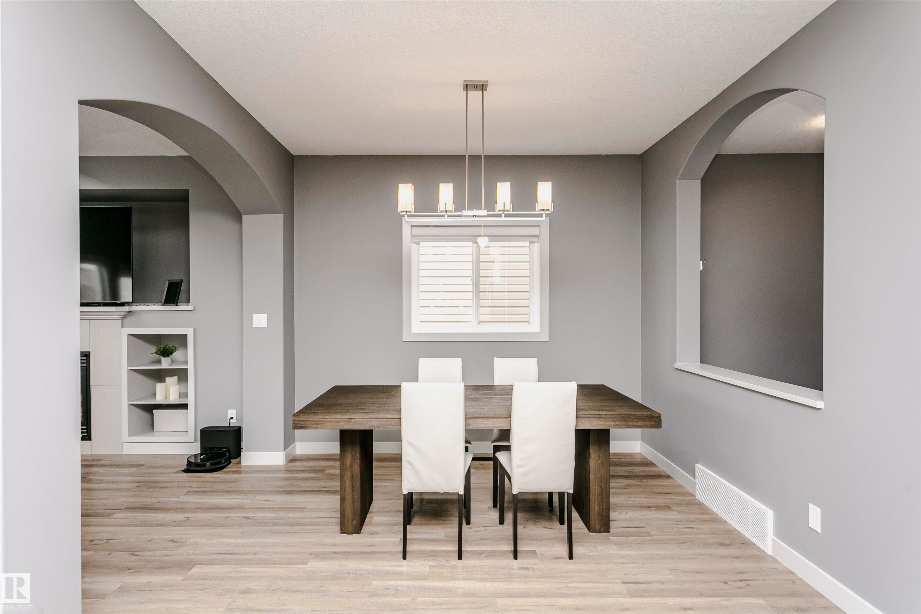 The property features an open-concept dining area with light-toned flooring, a window with horizontal blinds, and a modern rectangular chandelier - 21807 97 Avenue, Edmonton, AB - Indoor Photo Showing Dining Room