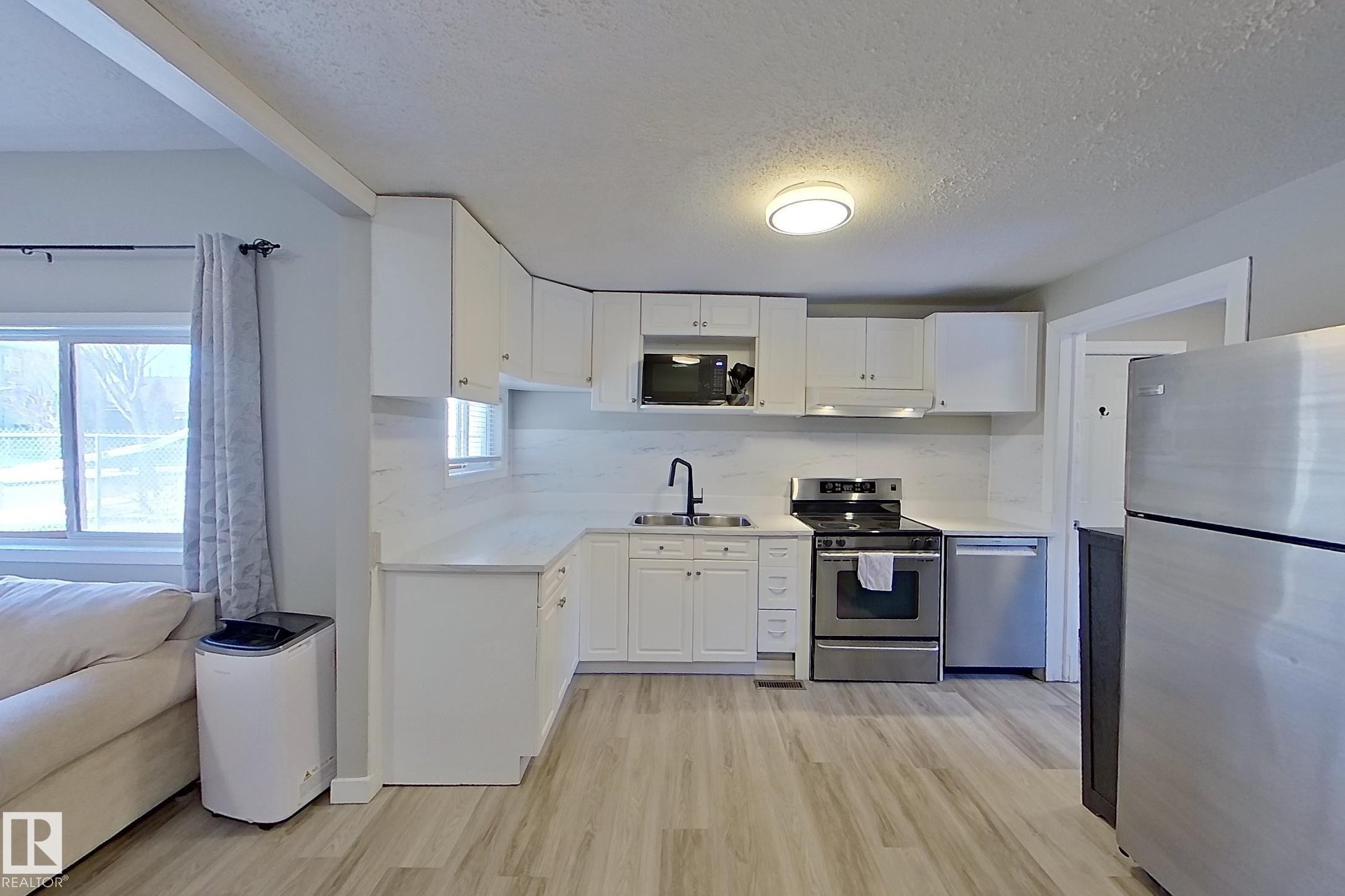 The property features a kitchen with white cabinetry, stainless steel appliances, and light-toned flooring - 9328 106A Avenue, Edmonton, AB - Indoor Photo Showing Kitchen With Double Sink