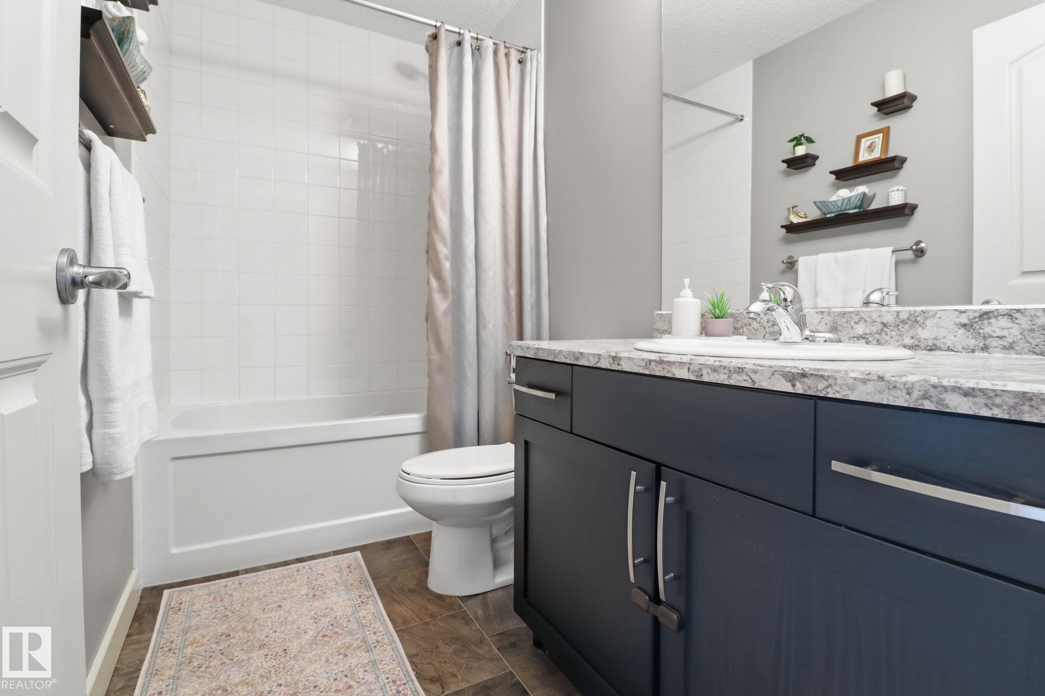 The bathroom features a deep blue vanity with a light-toned countertop, a white bathtub with white tiled walls, and a toilet - 430 Watt Boulevard, Edmonton, AB - Indoor Photo Showing Bathroom