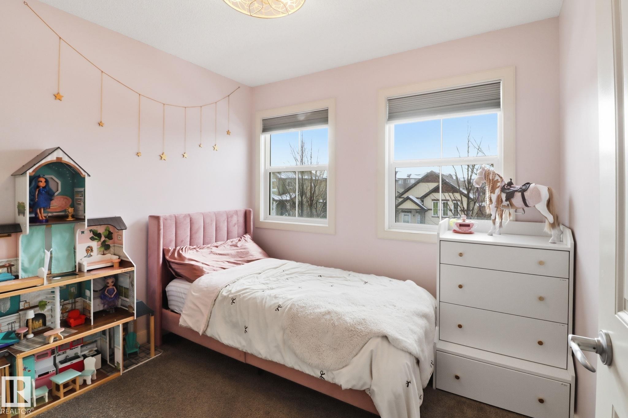 The property features a room with light pink walls, two windows, and dark-colored carpeting - 430 Watt Boulevard, Edmonton, AB - Indoor Photo Showing Bedroom