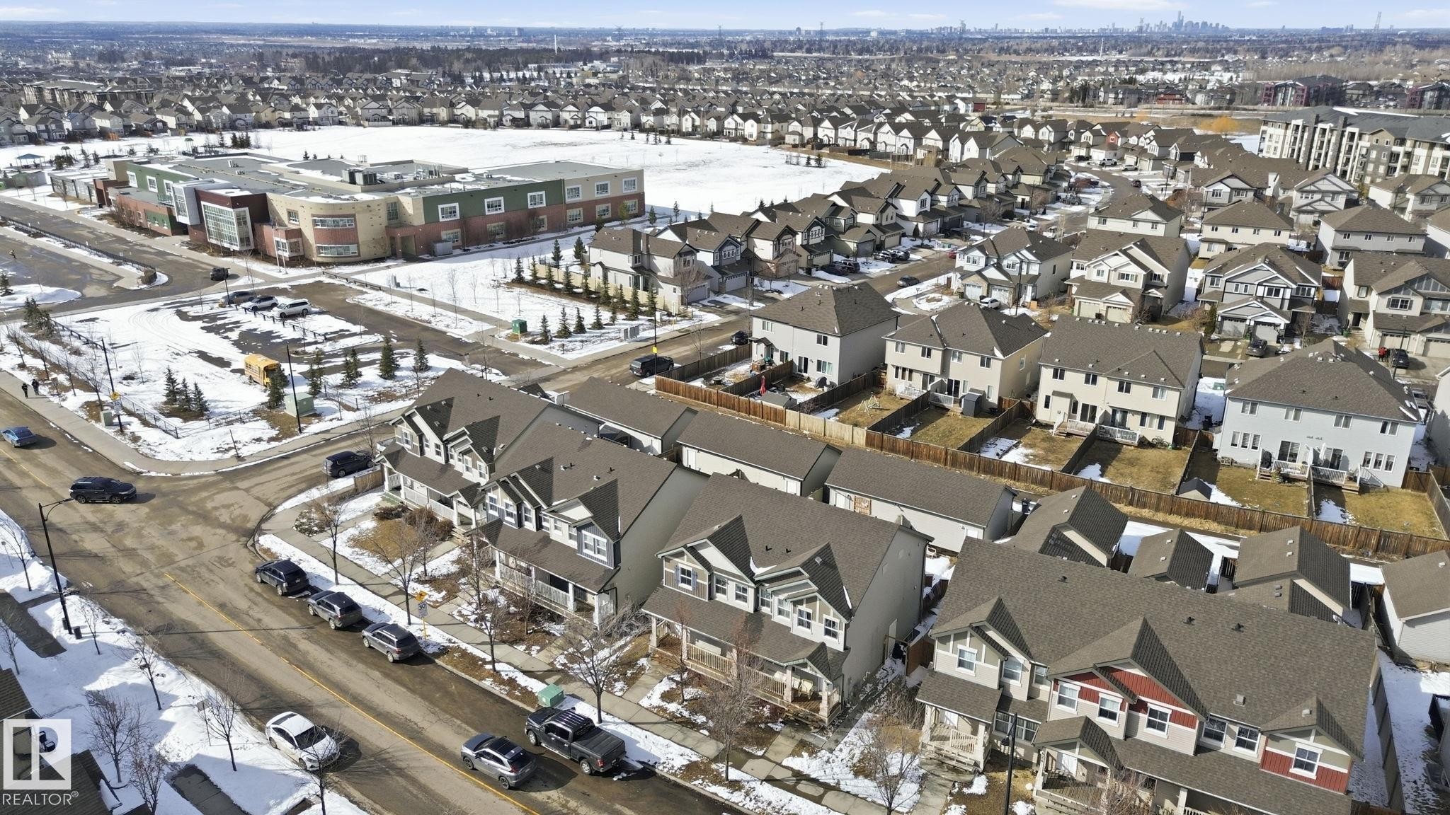Aerial view of the community, showcasing residential properties with fenced yards and a nearby building with a large field - 430 Watt Boulevard, Edmonton, AB - With View