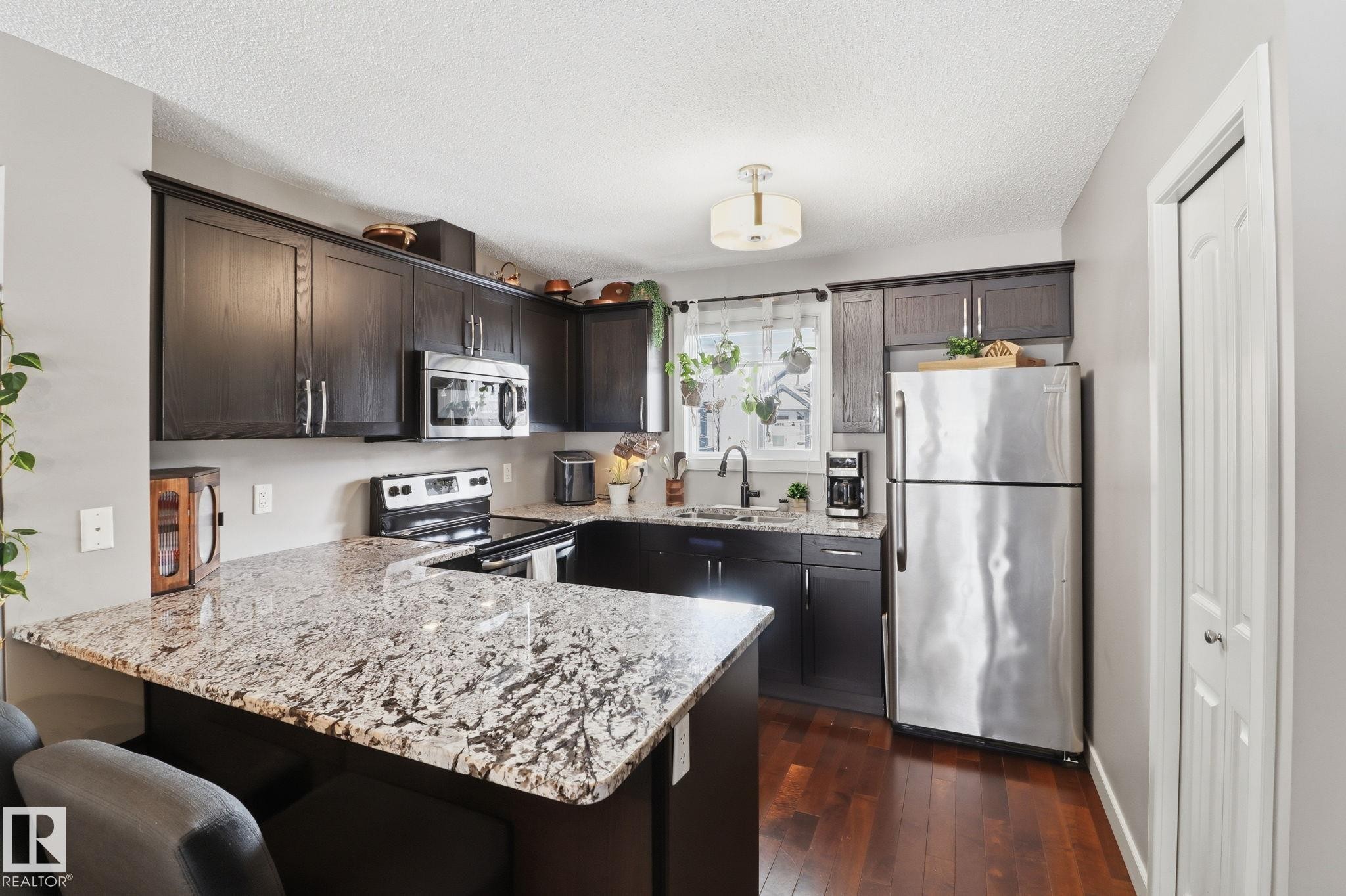 The kitchen features dark wood cabinetry, light-colored granite countertops, and stainless steel appliances - 430 Watt Boulevard, Edmonton, AB - Indoor Photo Showing Kitchen With Upgraded Kitchen