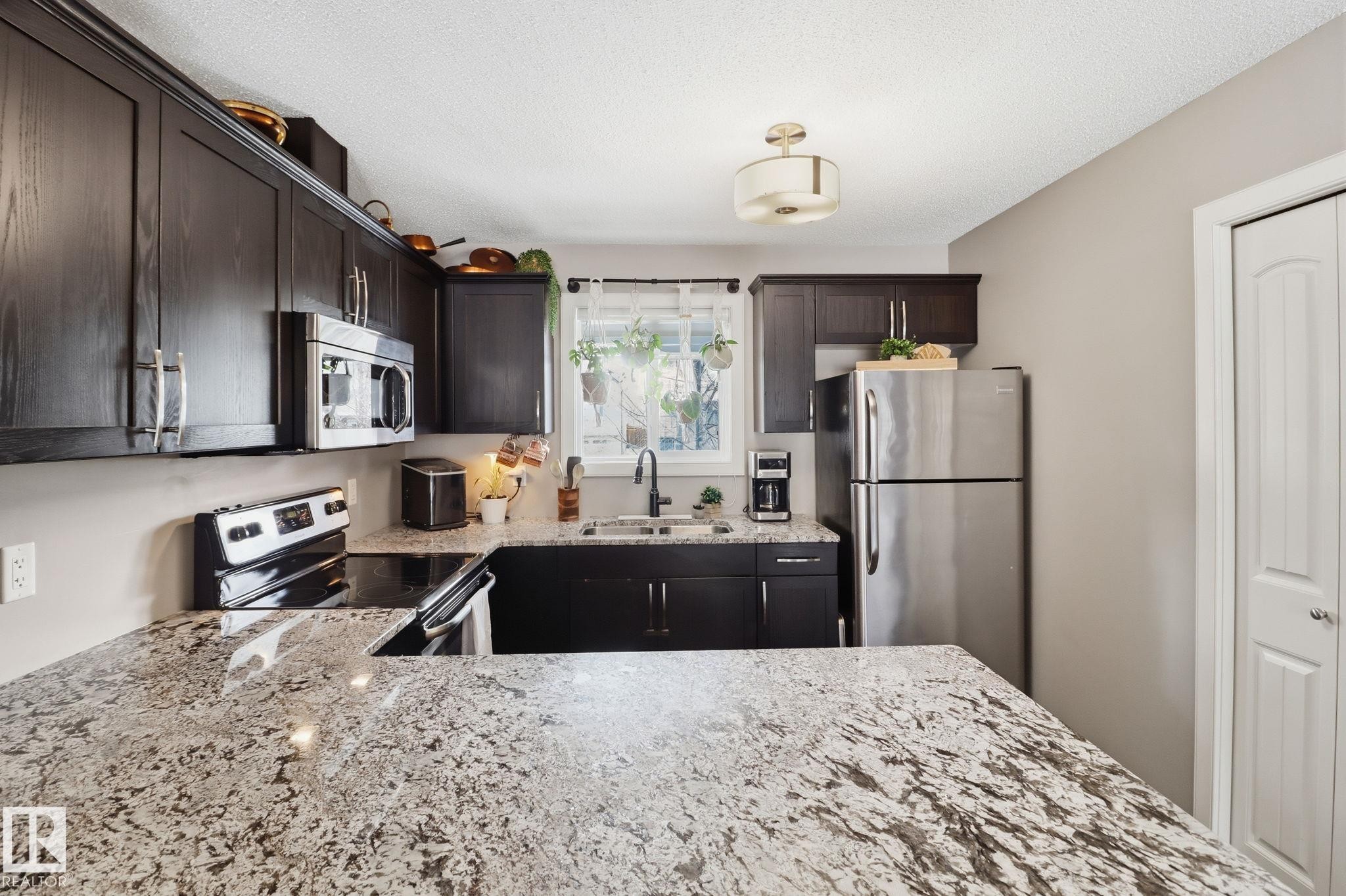 The kitchen features dark wood cabinetry, granite countertops, and stainless steel appliances, including a microwave, refrigerator, and electric range - 430 Watt Boulevard, Edmonton, AB - Indoor Photo Showing Kitchen