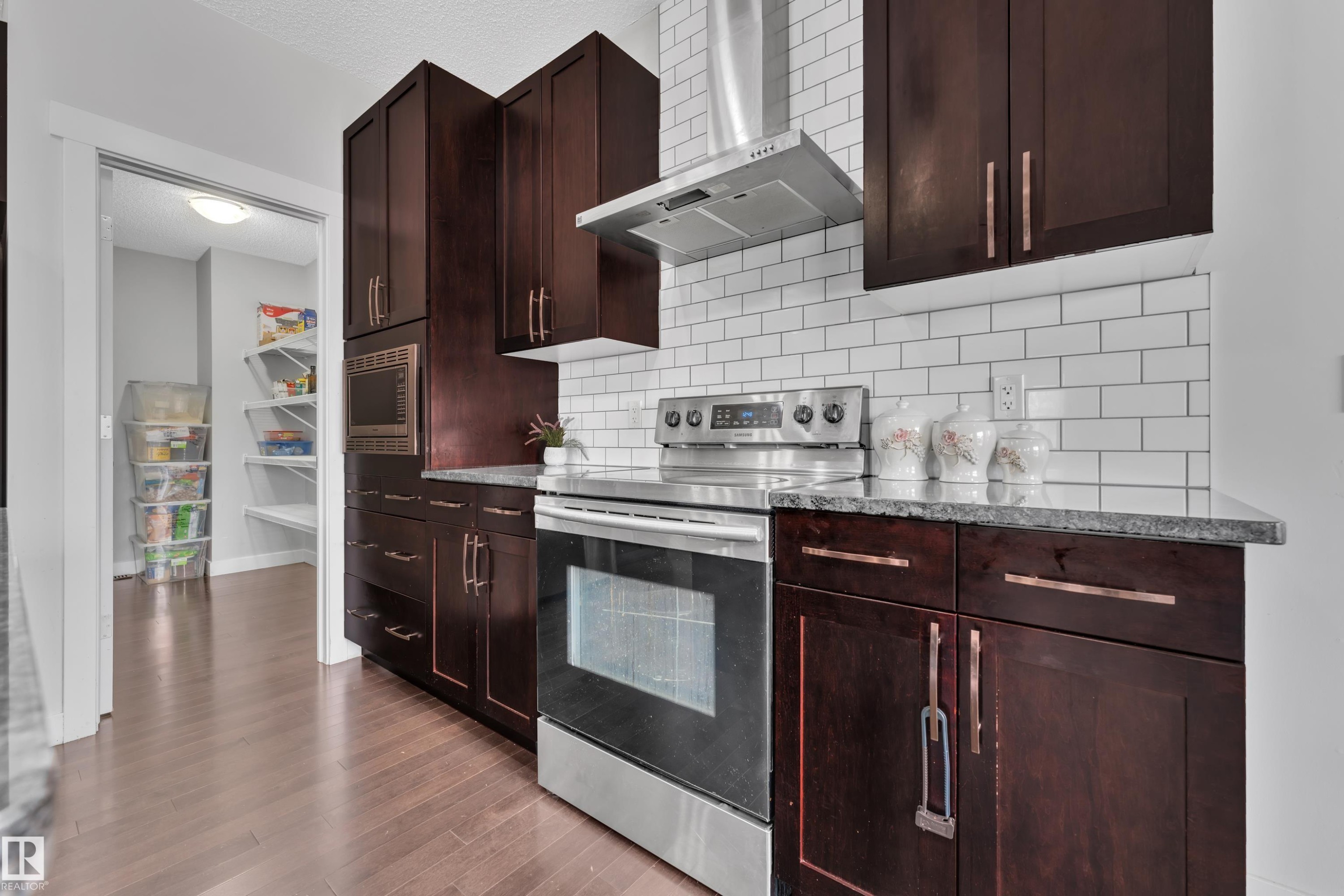 The kitchen features dark wood cabinetry, a stainless steel range with an overhead hood, and a white subway tile backsplash - 1452 30 Street, Edmonton, AB - Indoor Photo Showing Kitchen