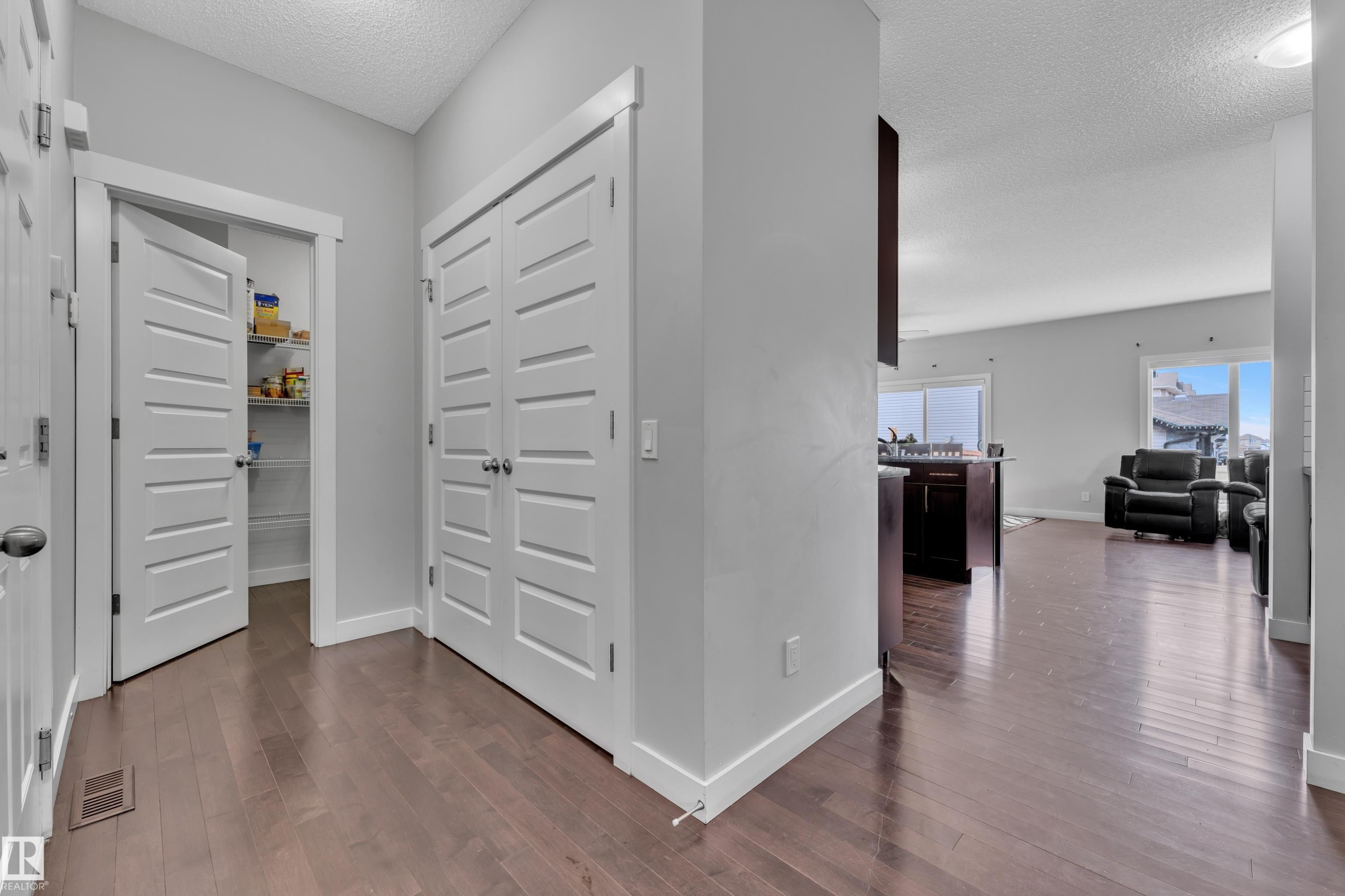 Hallway with hardwood floors, a pantry with shelving, and views into a living area with large windows - 1452 30 Street, Edmonton, AB - Indoor Photo Showing Other Room