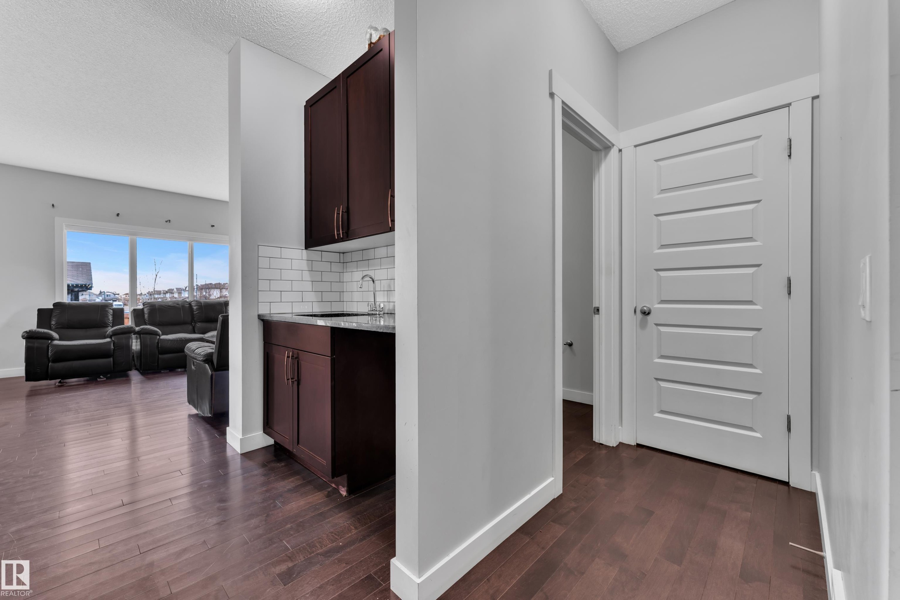 This property features rich hardwood flooring, a functional wet bar with dark cabinetry and subway tile backsplash, and a bright living area with large windows - 1452 30 Street, Edmonton, AB - Indoor Photo Showing Other Room
