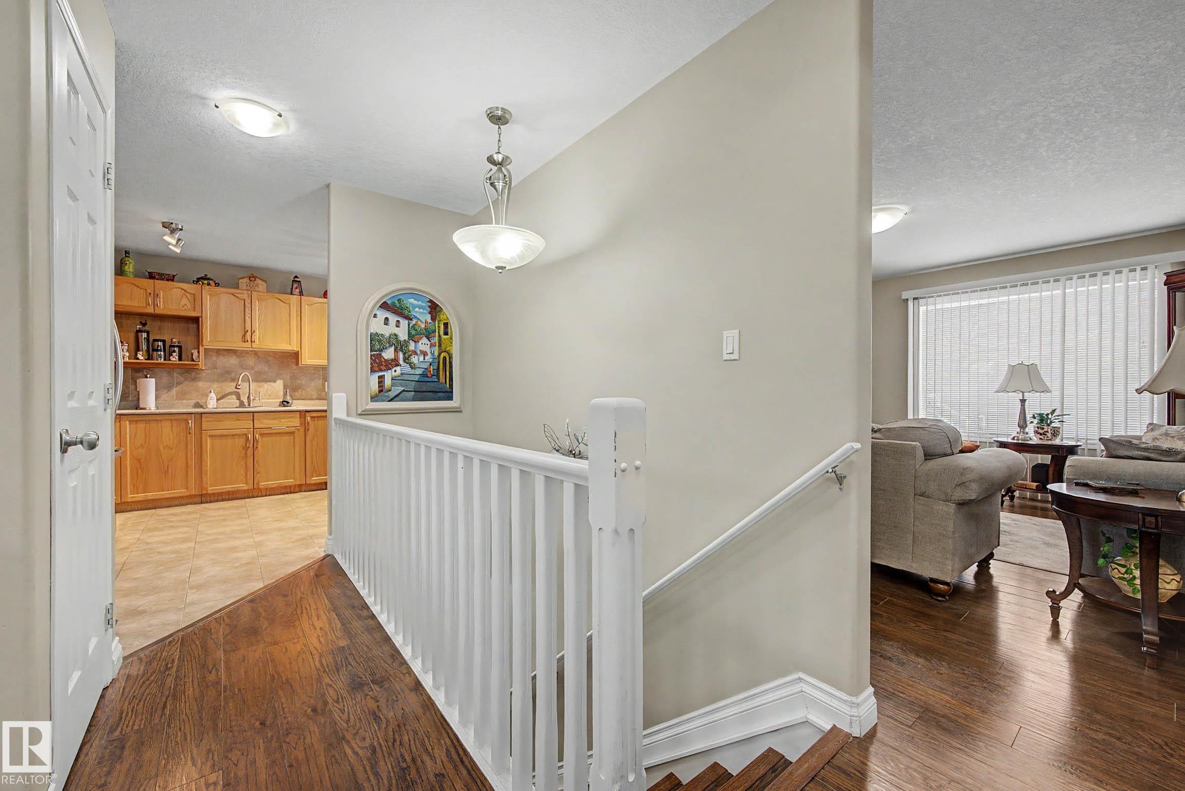 The property features hardwood flooring in the main living areas, a staircase with white railings, and a kitchen with light wood cabinetry and light-colored tiled floors - 21 1850 Mill Woods Road E, Edmonton, AB - Indoor