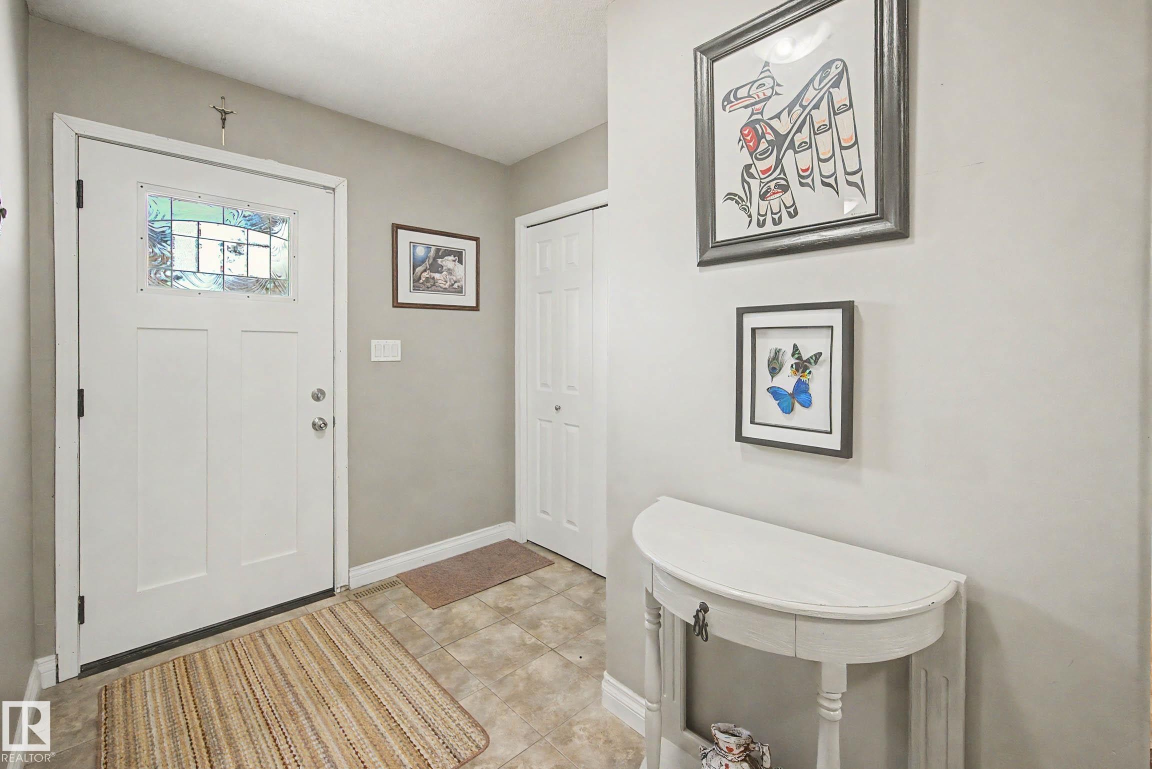 The entry features a white door with a stained glass insert, tile flooring, and light-colored walls - 21 1850 Mill Woods Road E, Edmonton, AB - Indoor Photo Showing Other Room