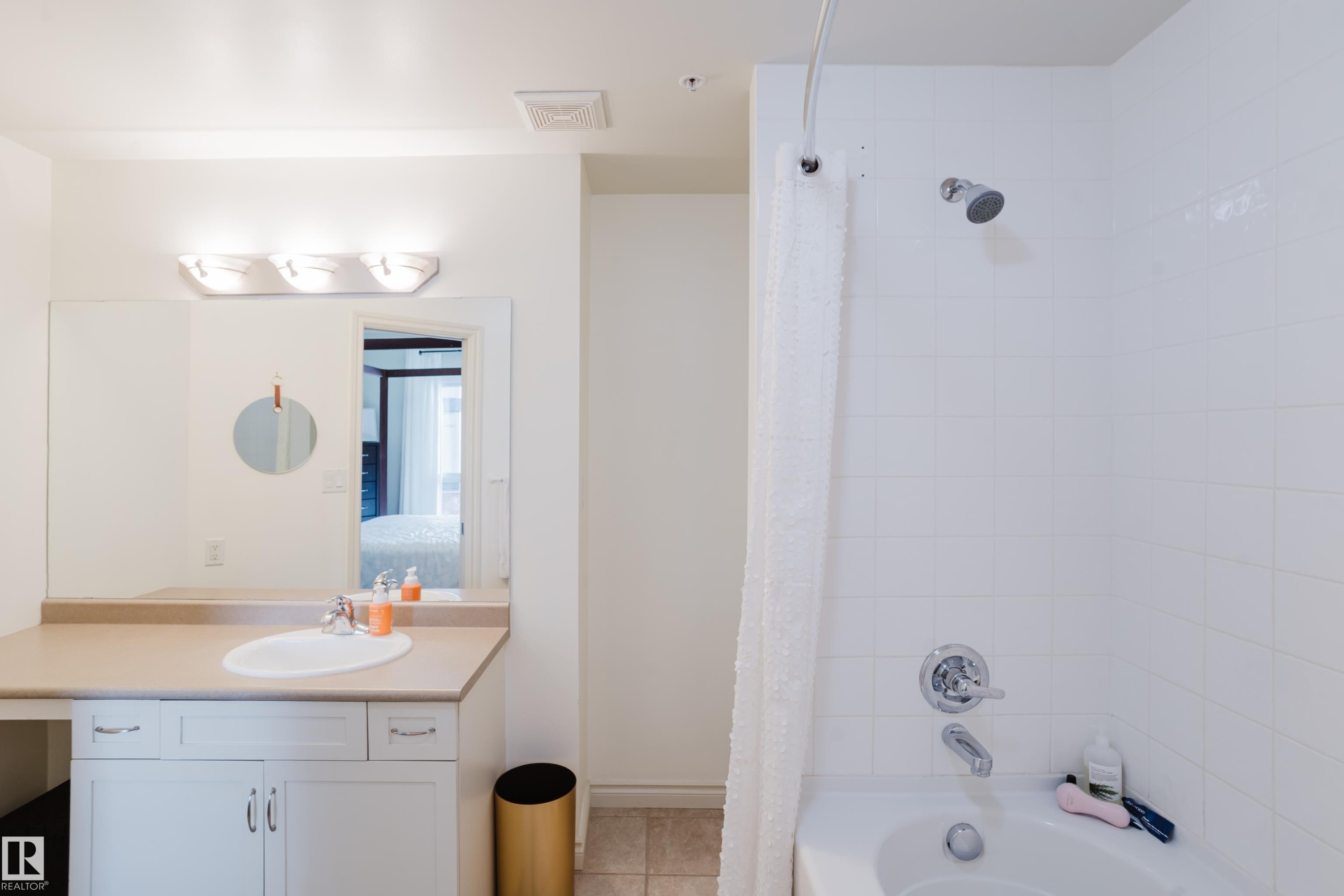 The bathroom features a vanity with an integrated sink, a large mirror, and a three-light fixture - 206 10108 125 Street, Edmonton, AB - Indoor Photo Showing Bathroom