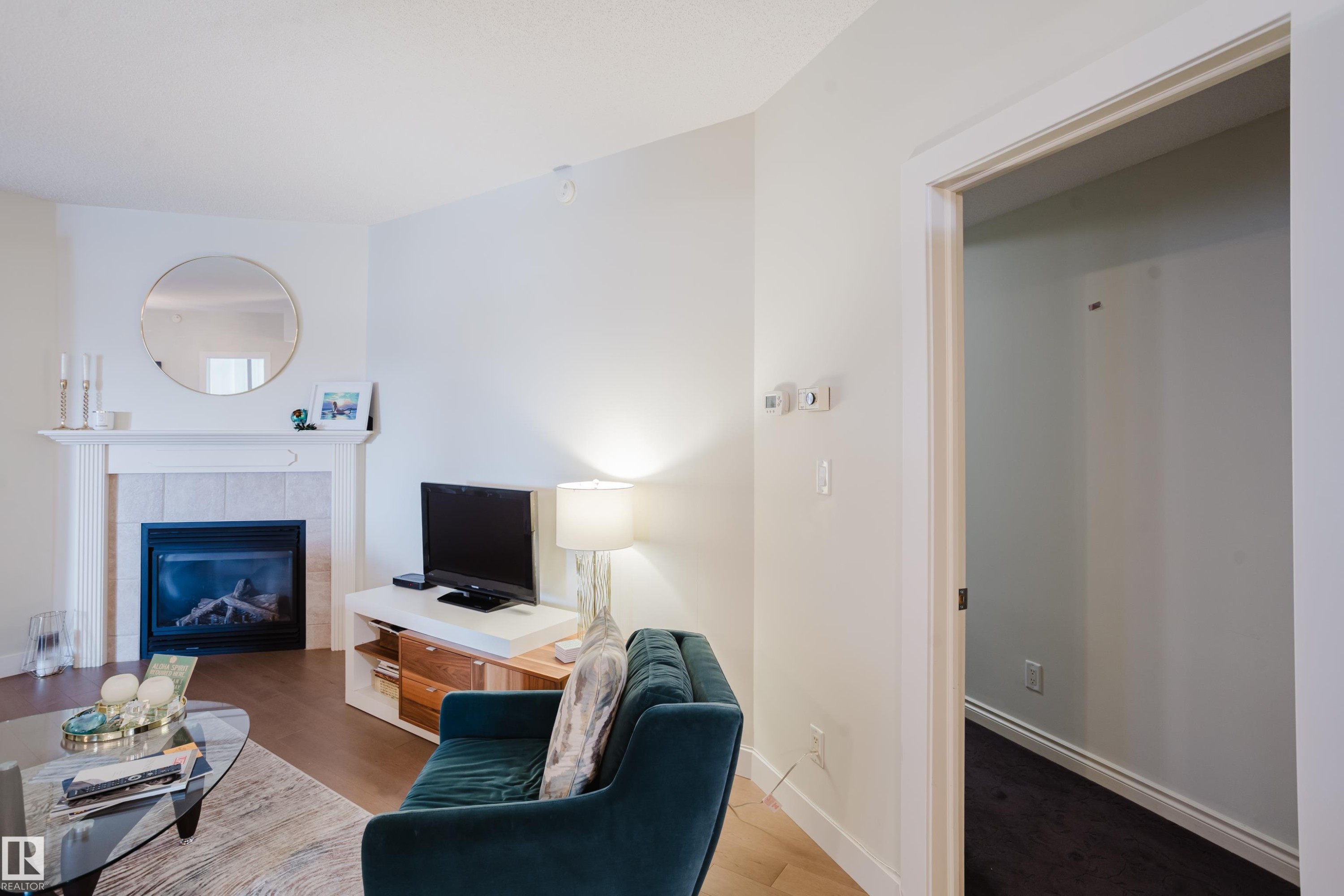 The living area features hardwood flooring, a fireplace with a white mantel, and a rounded mirror - 206 10108 125 Street, Edmonton, AB - Indoor Photo Showing Living Room With Fireplace
