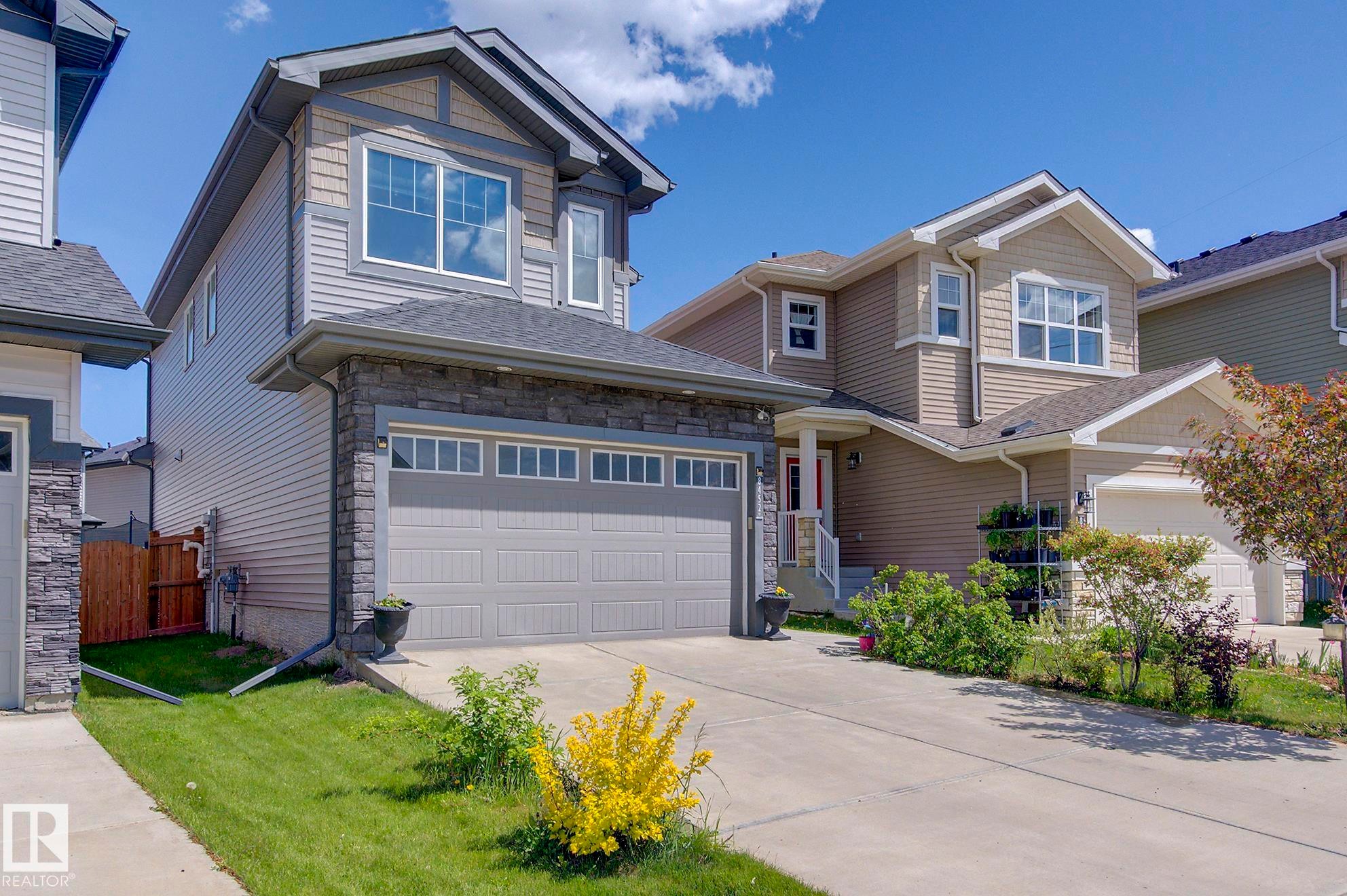 The property features a two-story exterior with siding and stone accents, a double garage, and a concrete driveway - 8452 Cushing Crest, Edmonton, AB - Outdoor With Facade