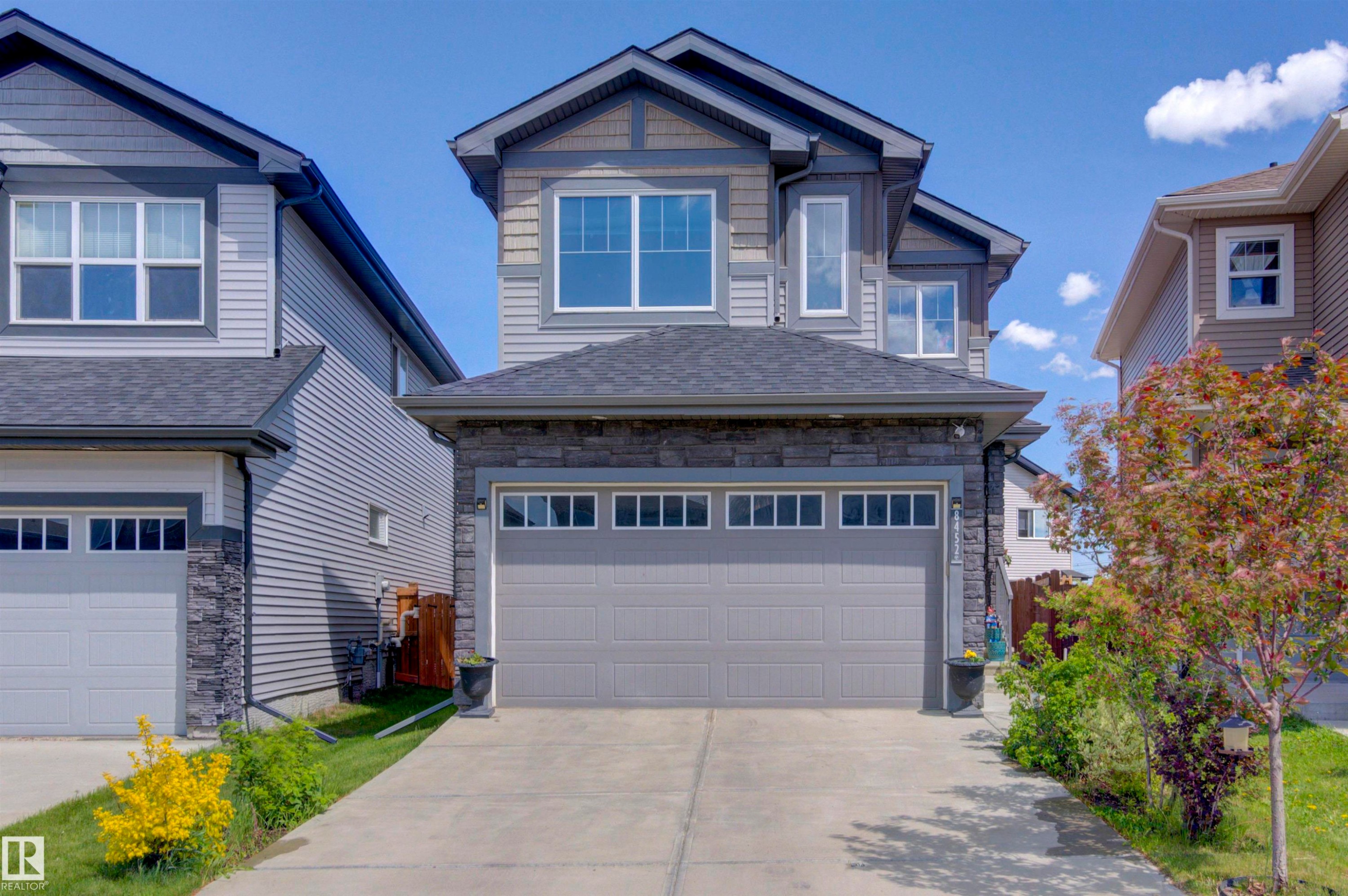 The property features a dark gray garage door, a stone facade, and a paved driveway - 8452 Cushing Crest, Edmonton, AB - Outdoor With Facade