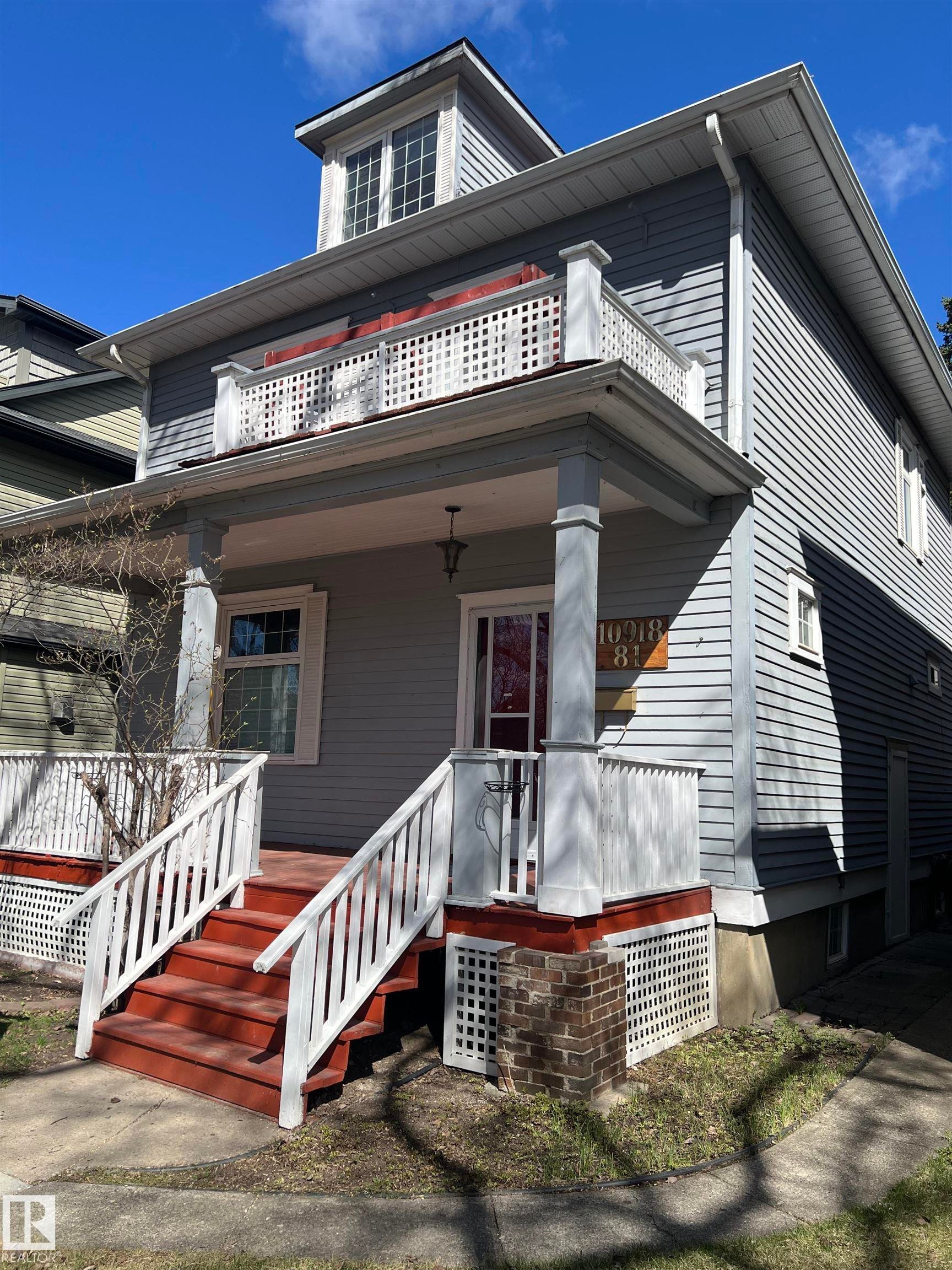 Exterior featuring dormer windows, a second-story balcony with white lattice railing, a covered porch with square columns, and a red-painted front stairway with white railings - 10918 81 Avenue, Edmonton, AB - Outdoor With Exterior