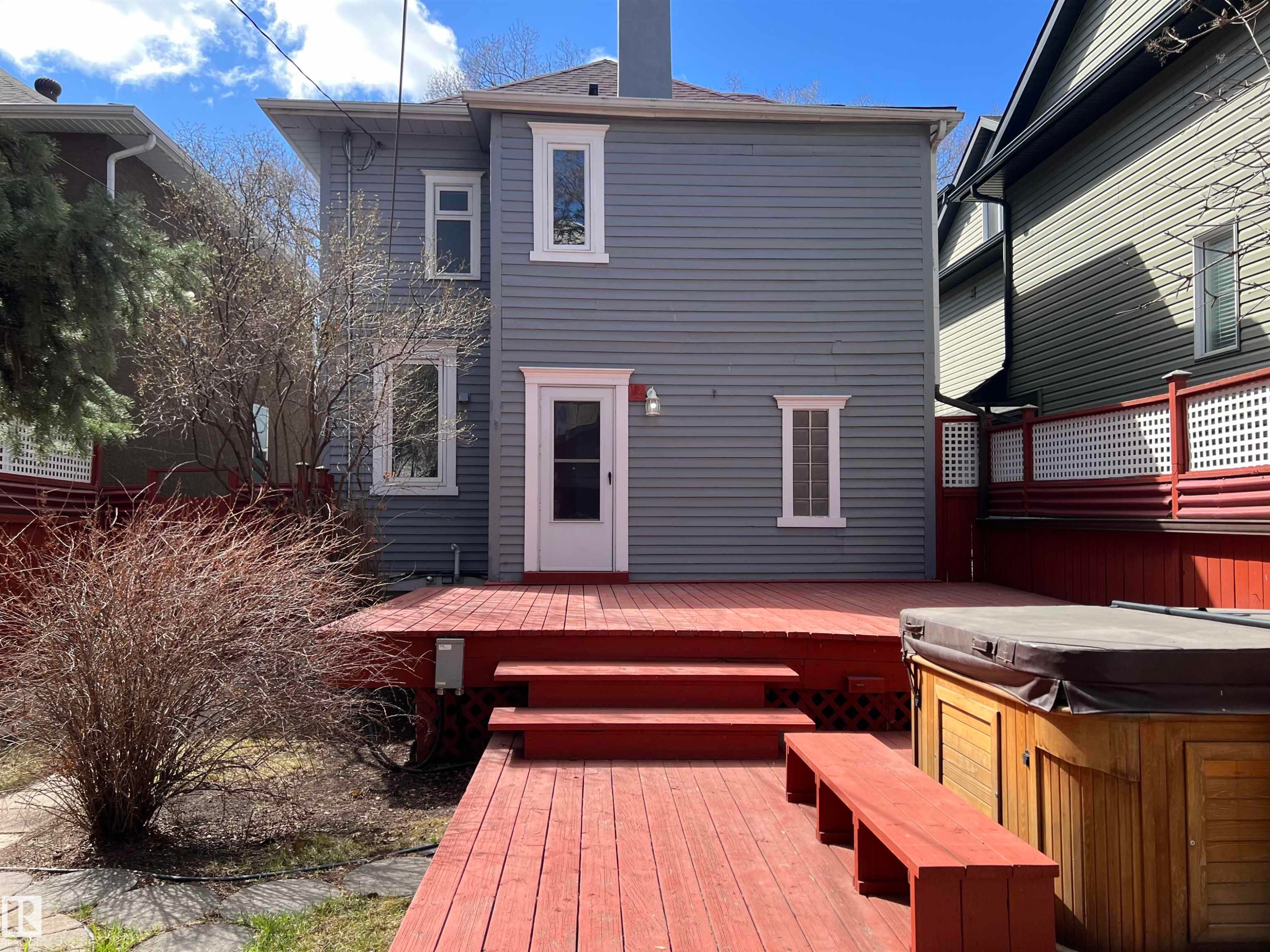 Rear exterior featuring gray siding, white trim, a red-stained multi-level deck, built-in wooden bench seating, and a hot tub - 10918 81 Avenue, Edmonton, AB - Outdoor With Exterior