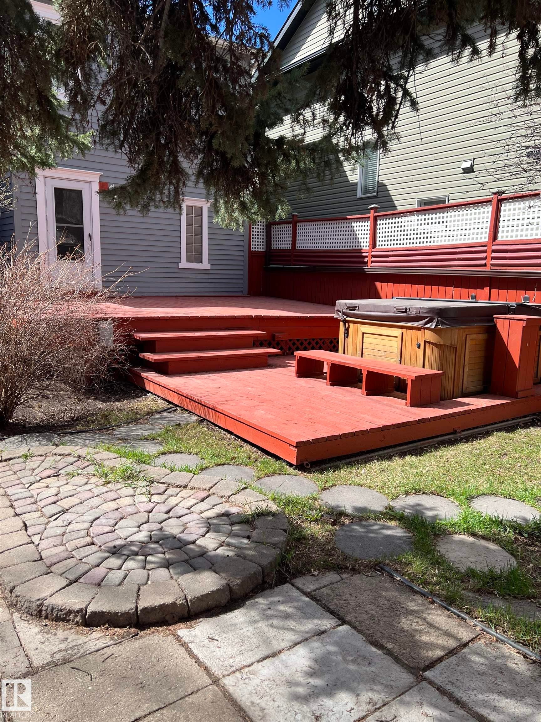 Red-stained multi-level wood deck featuring an integrated hot tub and decorative lattice railing - 10918 81 Avenue, Edmonton, AB - Outdoor