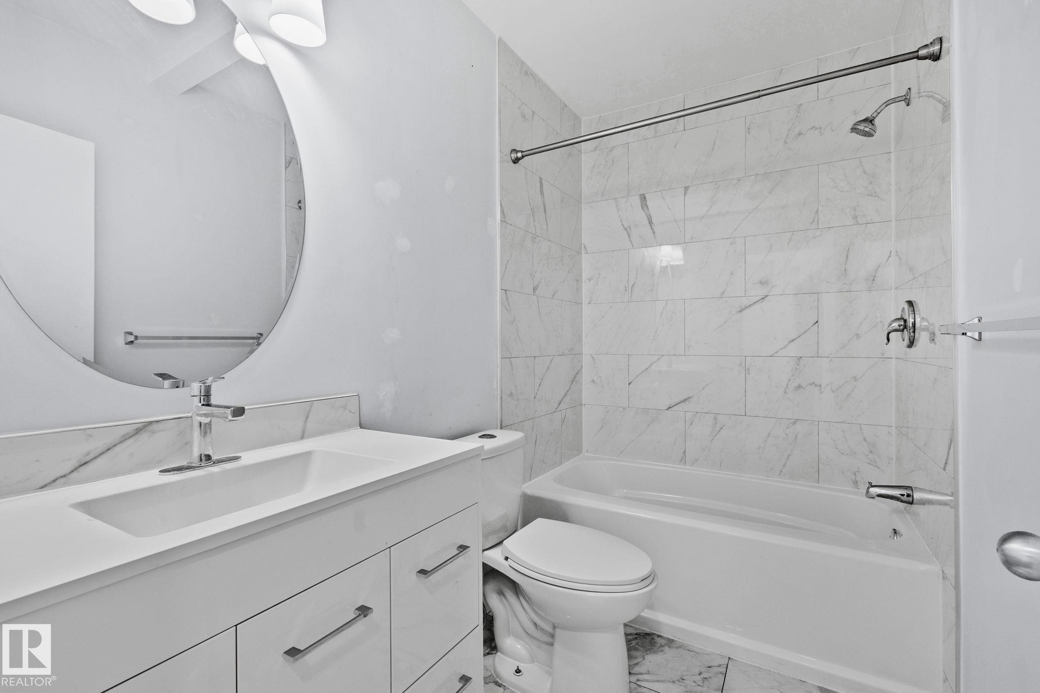 The bathroom features a white vanity with a rectangular sink, a round wall-mounted mirror, and a toilet - 12002 37 Street, Edmonton, AB - Indoor Photo Showing Bathroom
