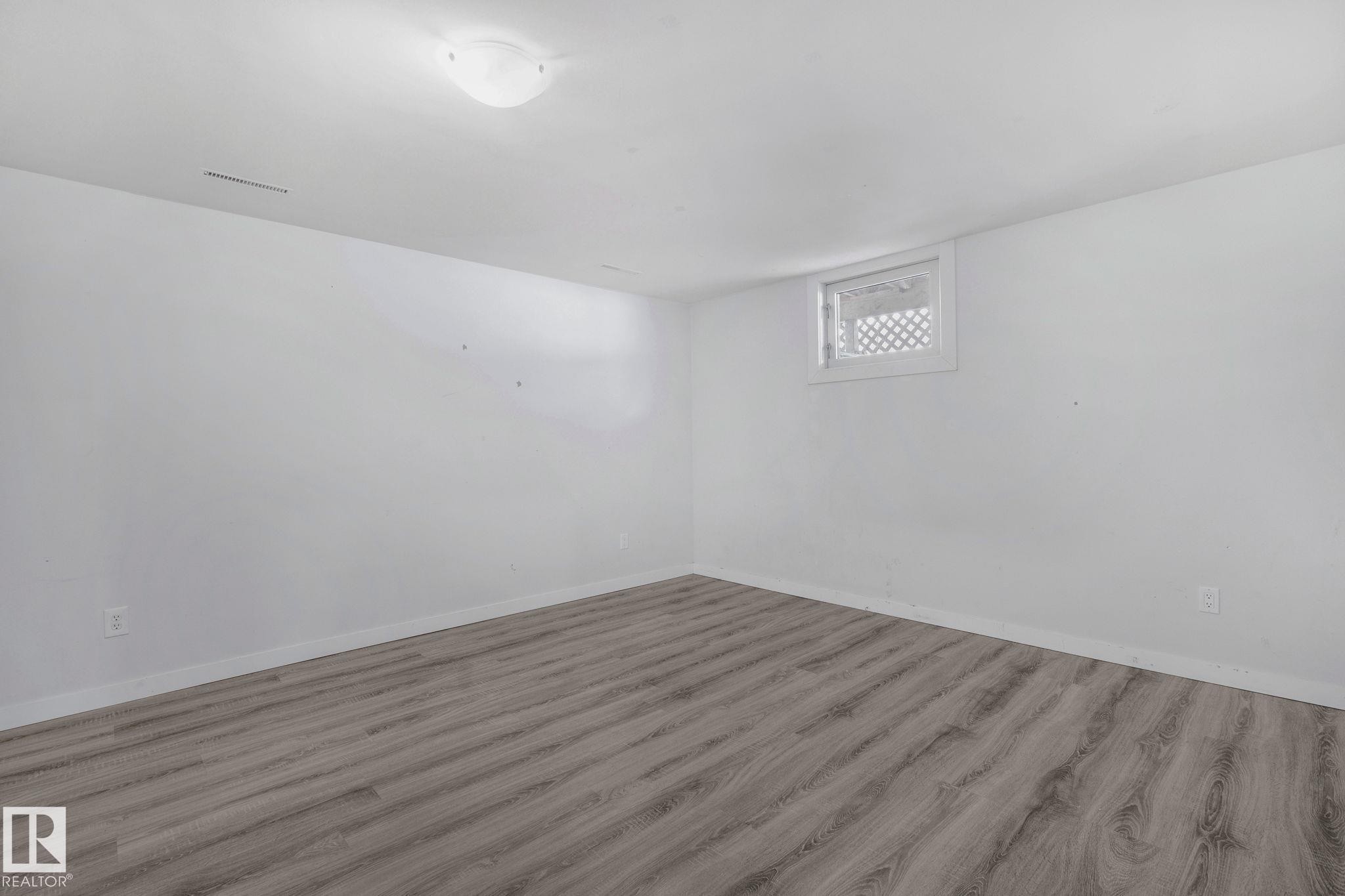 This room features light-toned flooring, white walls, and a window with a lattice-style grate - 12002 37 Street, Edmonton, AB - Indoor Photo Showing Other Room
